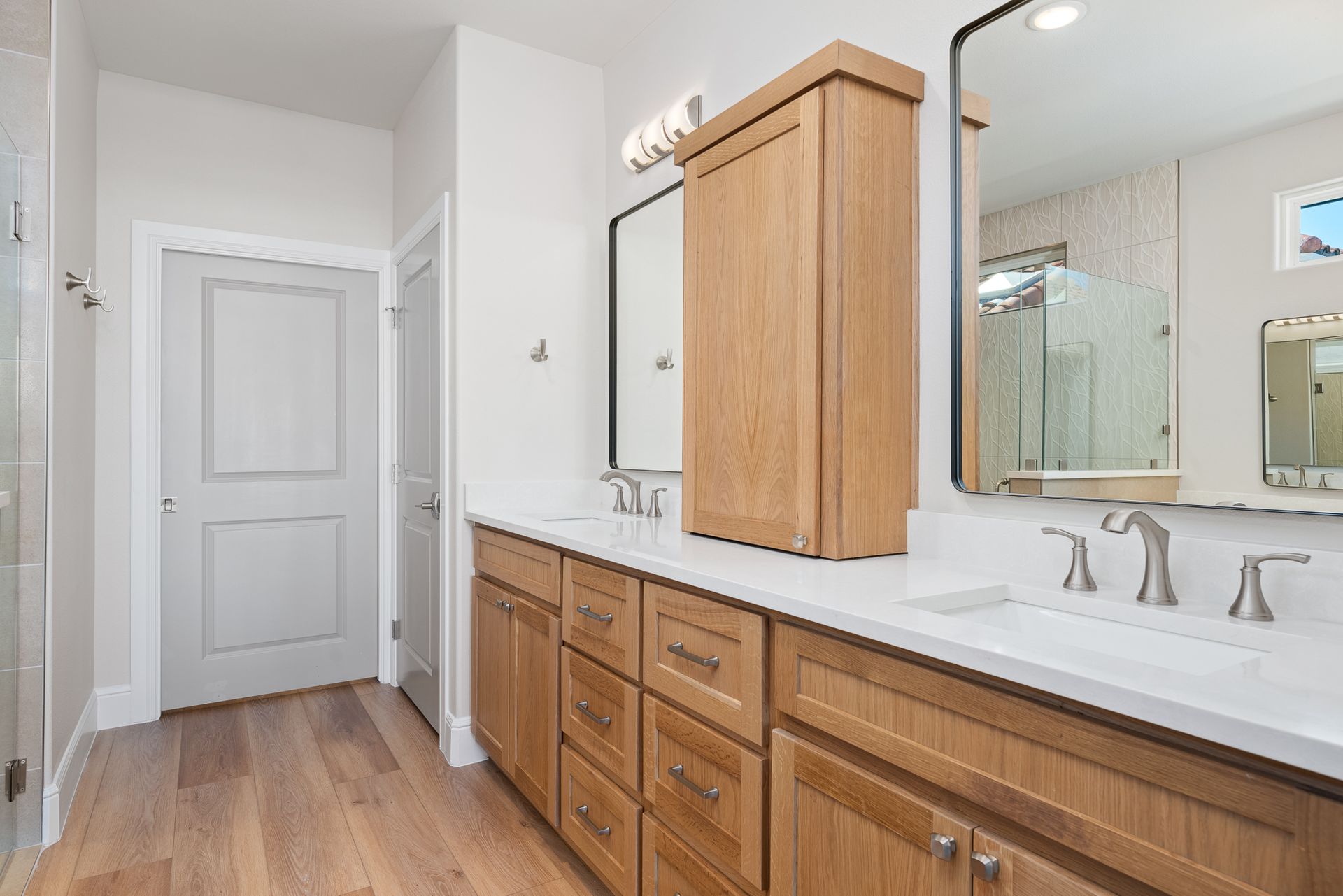 A bathroom with two sinks , two mirrors , and wooden cabinets.