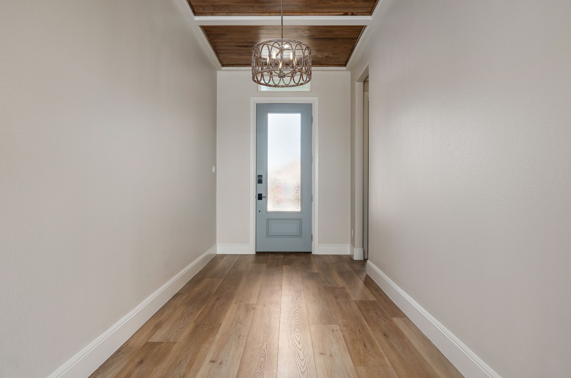 An empty hallway with a blue door and a chandelier hanging from the ceiling.