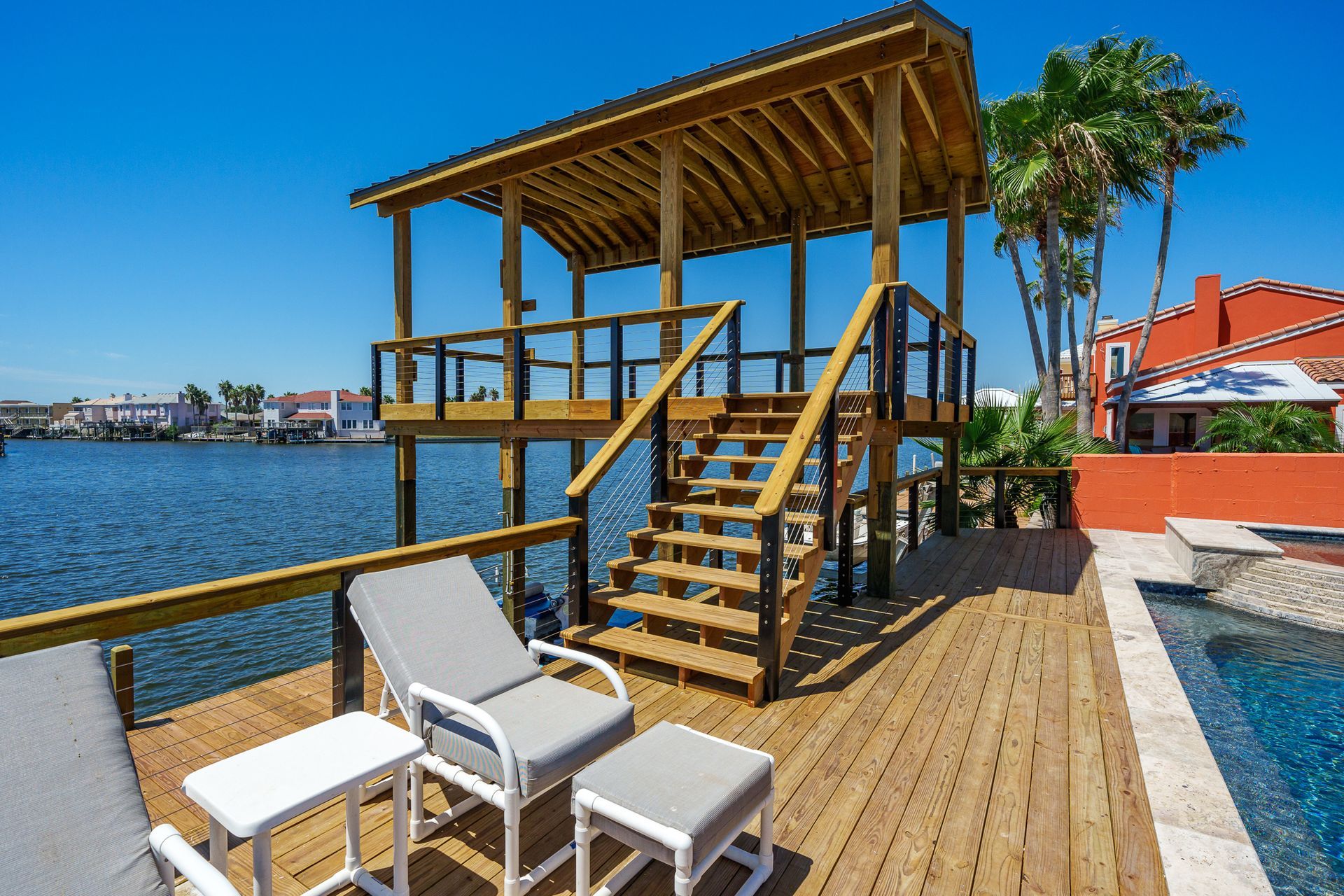 A wooden deck with chairs and tables overlooking a body of water.