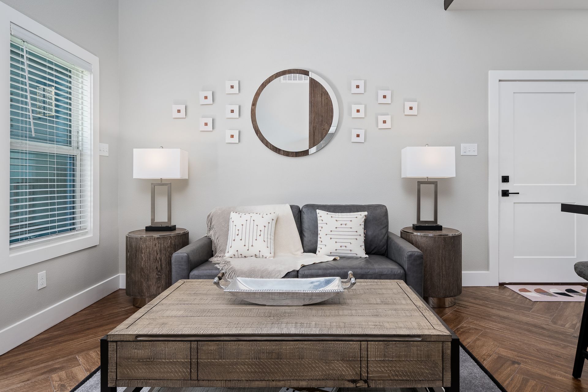A living room with a couch , coffee table , lamps and a mirror on the wall.
