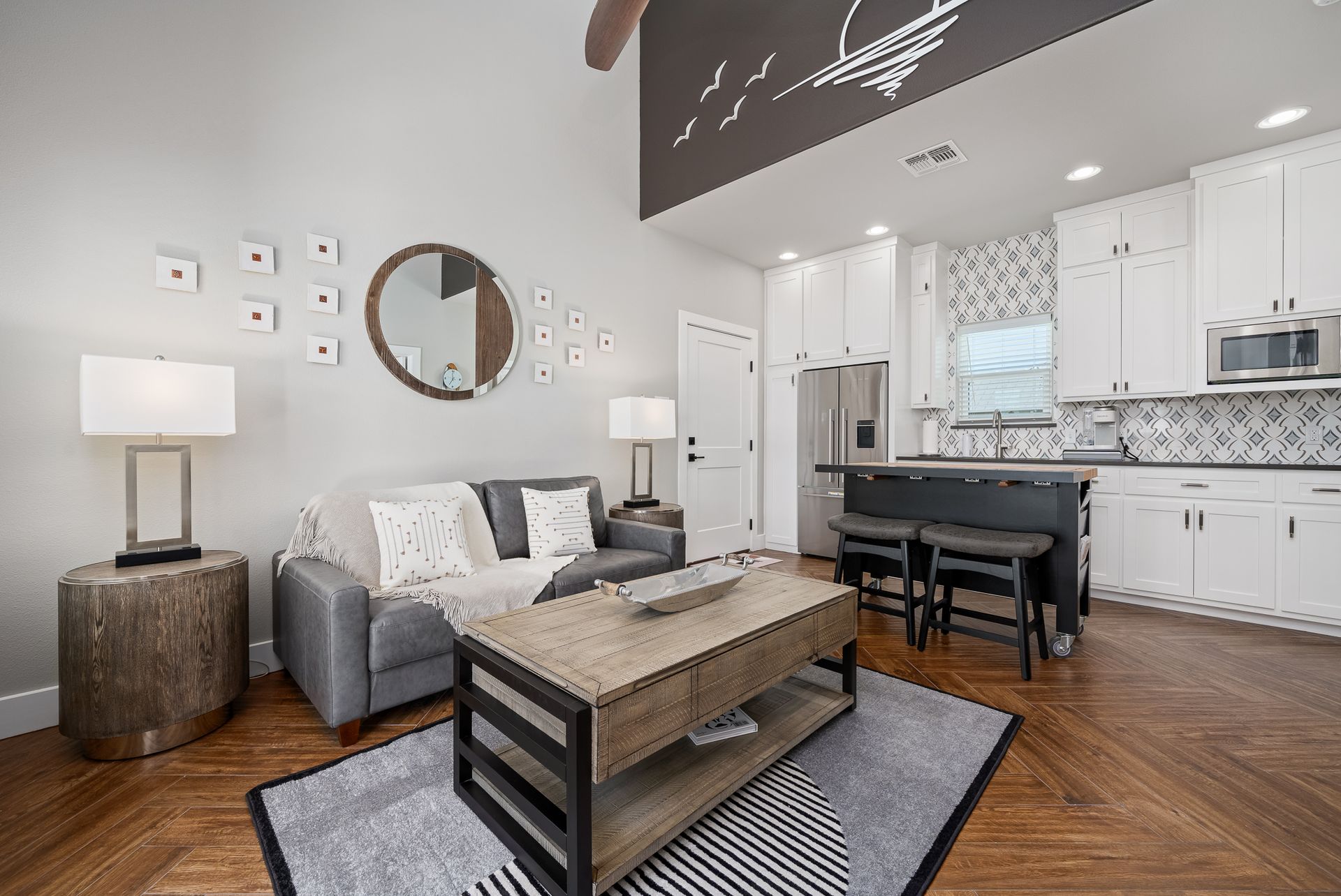 A living room with a couch , coffee table , lamps and a kitchen.