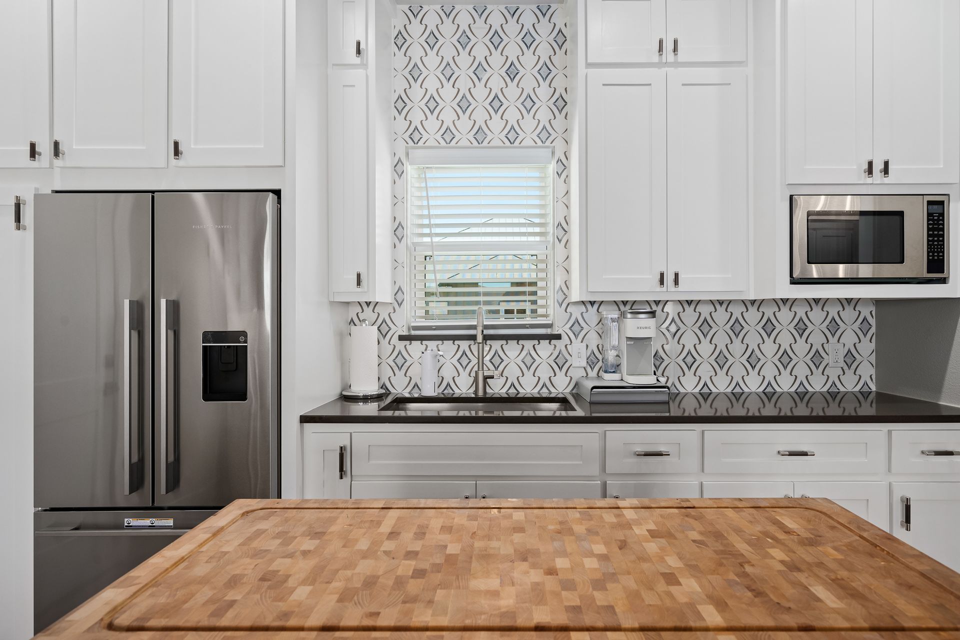 A kitchen with white cabinets , a stainless steel refrigerator , a sink , and a wooden counter top.