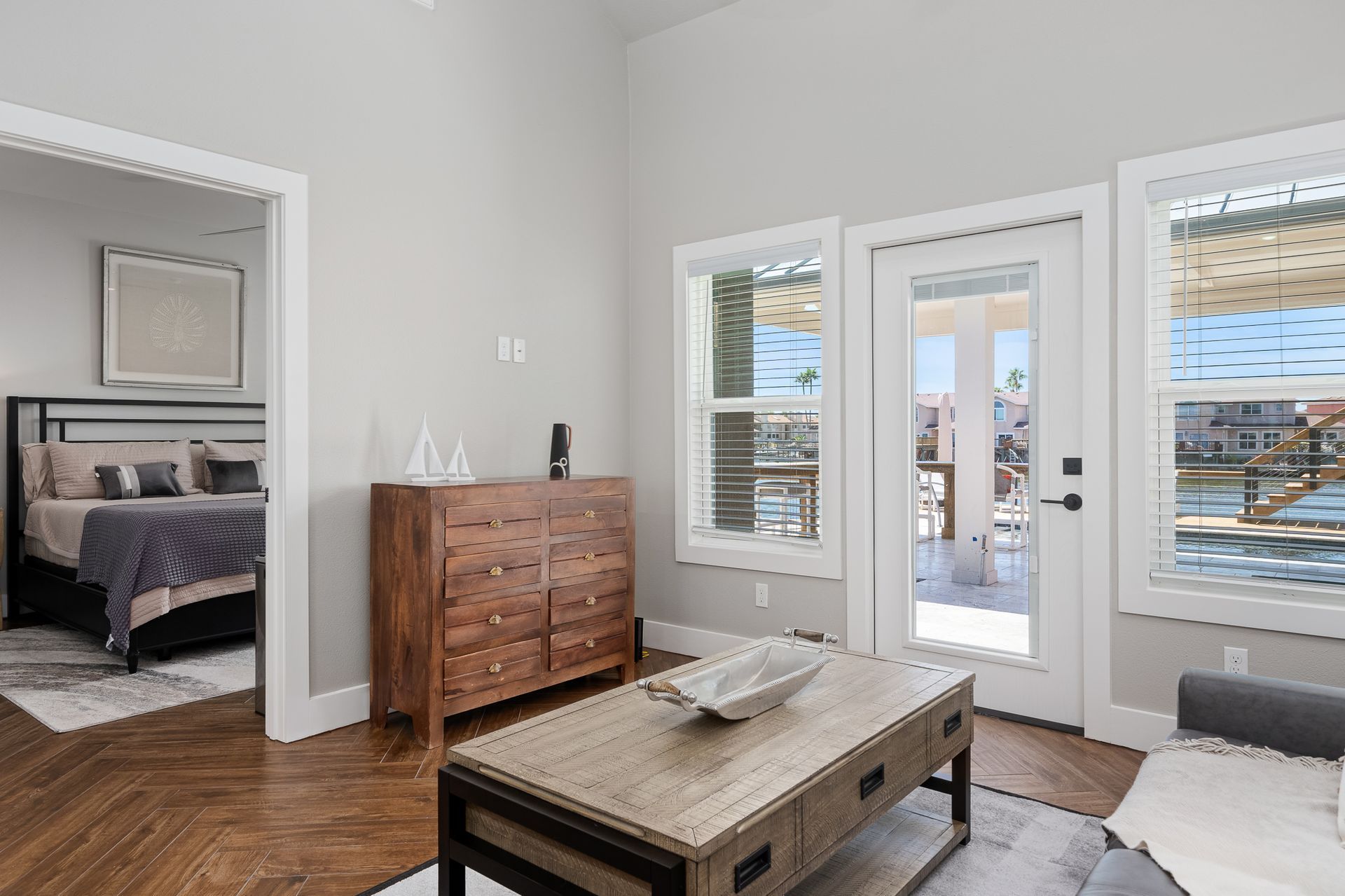 A living room with a coffee table , dresser , and sliding glass doors leading to a bedroom.