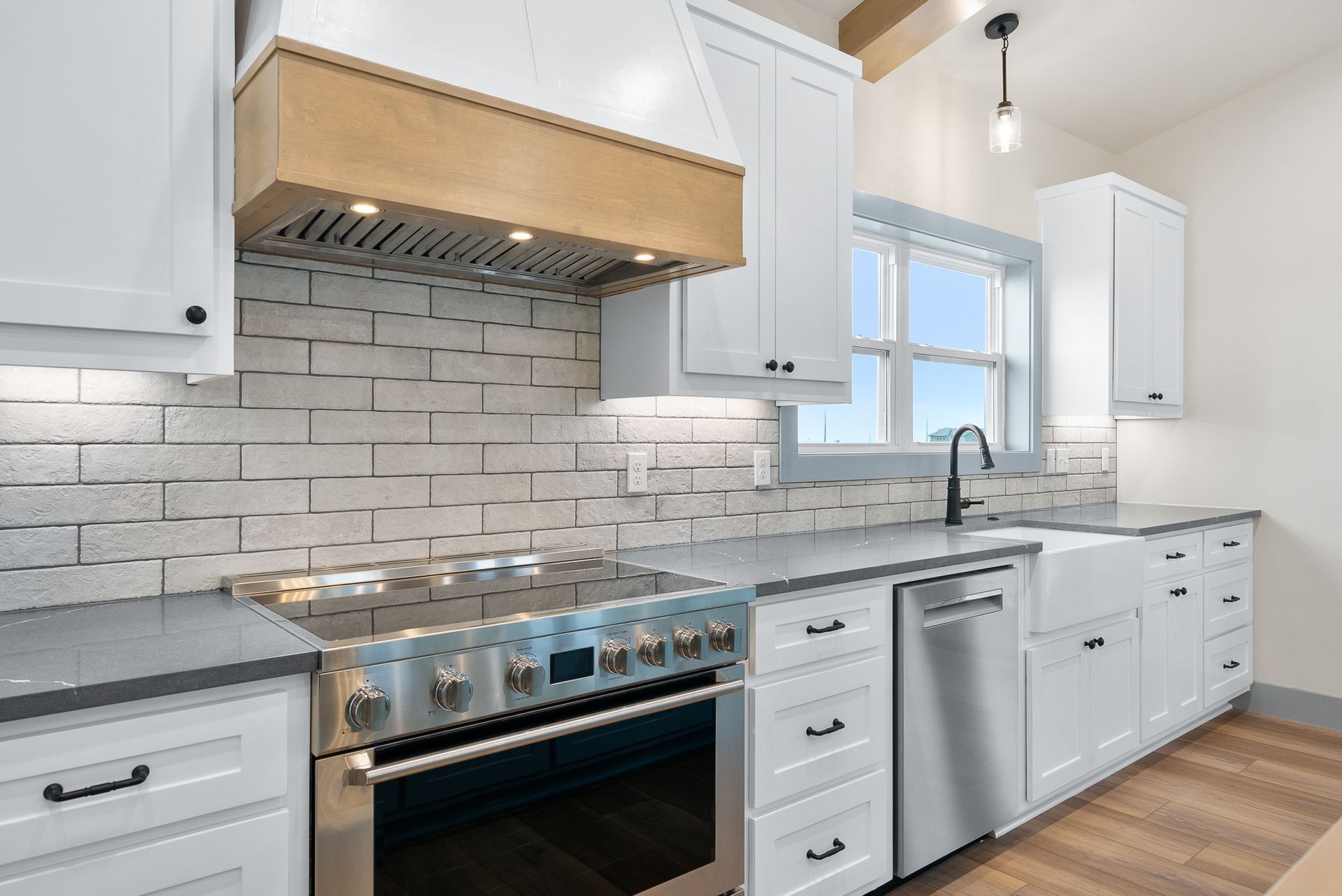 White kitchen with stainless steel appliances, white cabinets, and light wood range hood.
