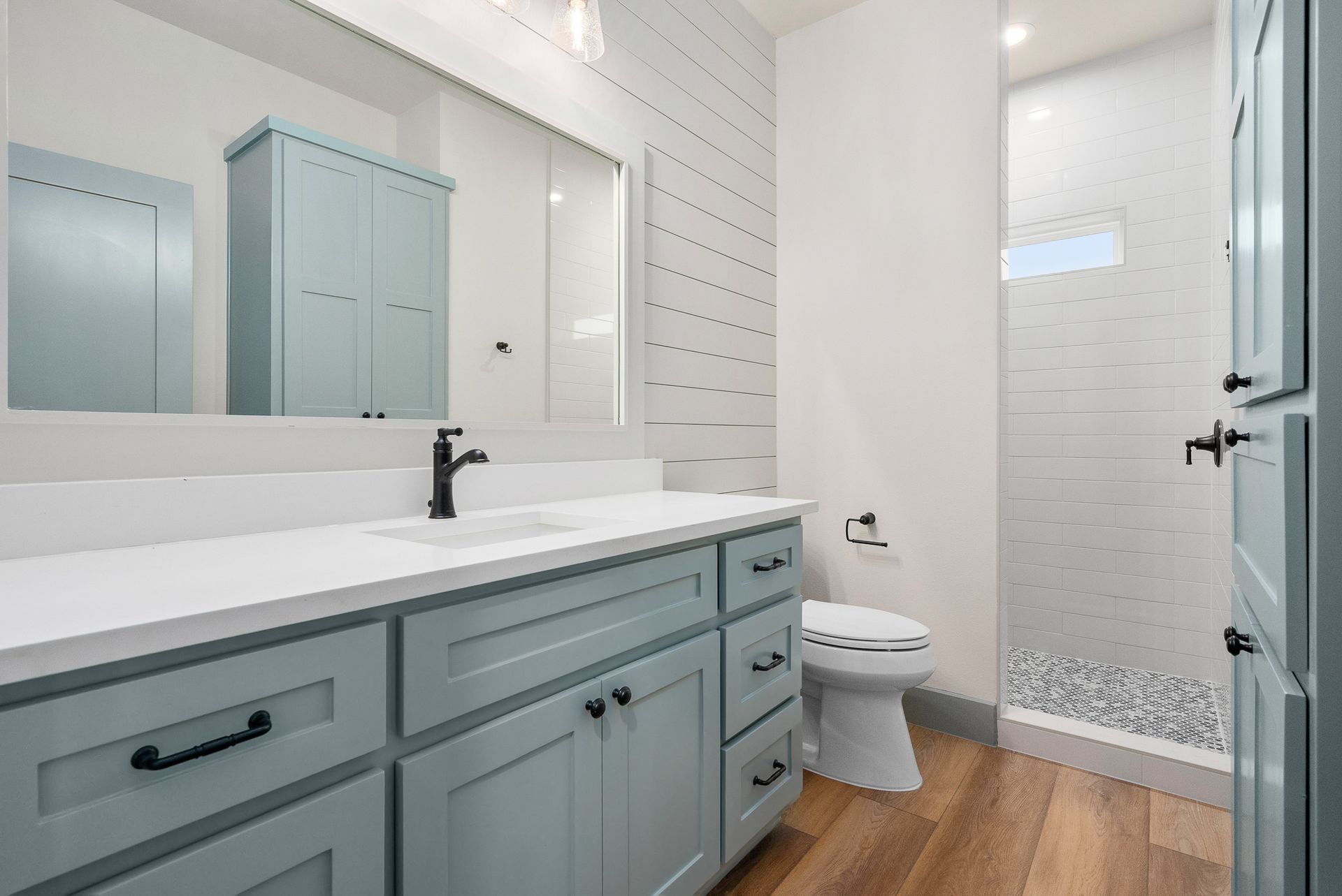 Bathroom with blue vanity, white countertop, and wood-look flooring. Includes a shower and cabinet.