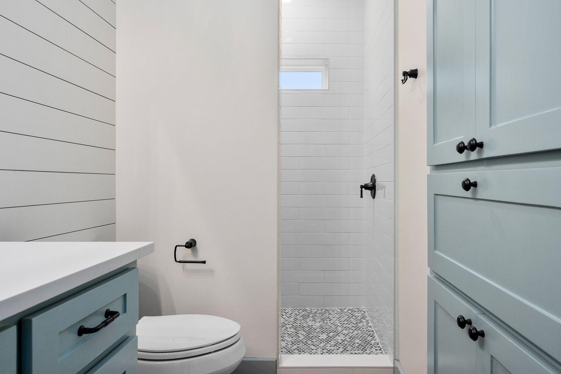 Bathroom with blue cabinets, white shiplap walls, shower with pebble floor, and toilet.