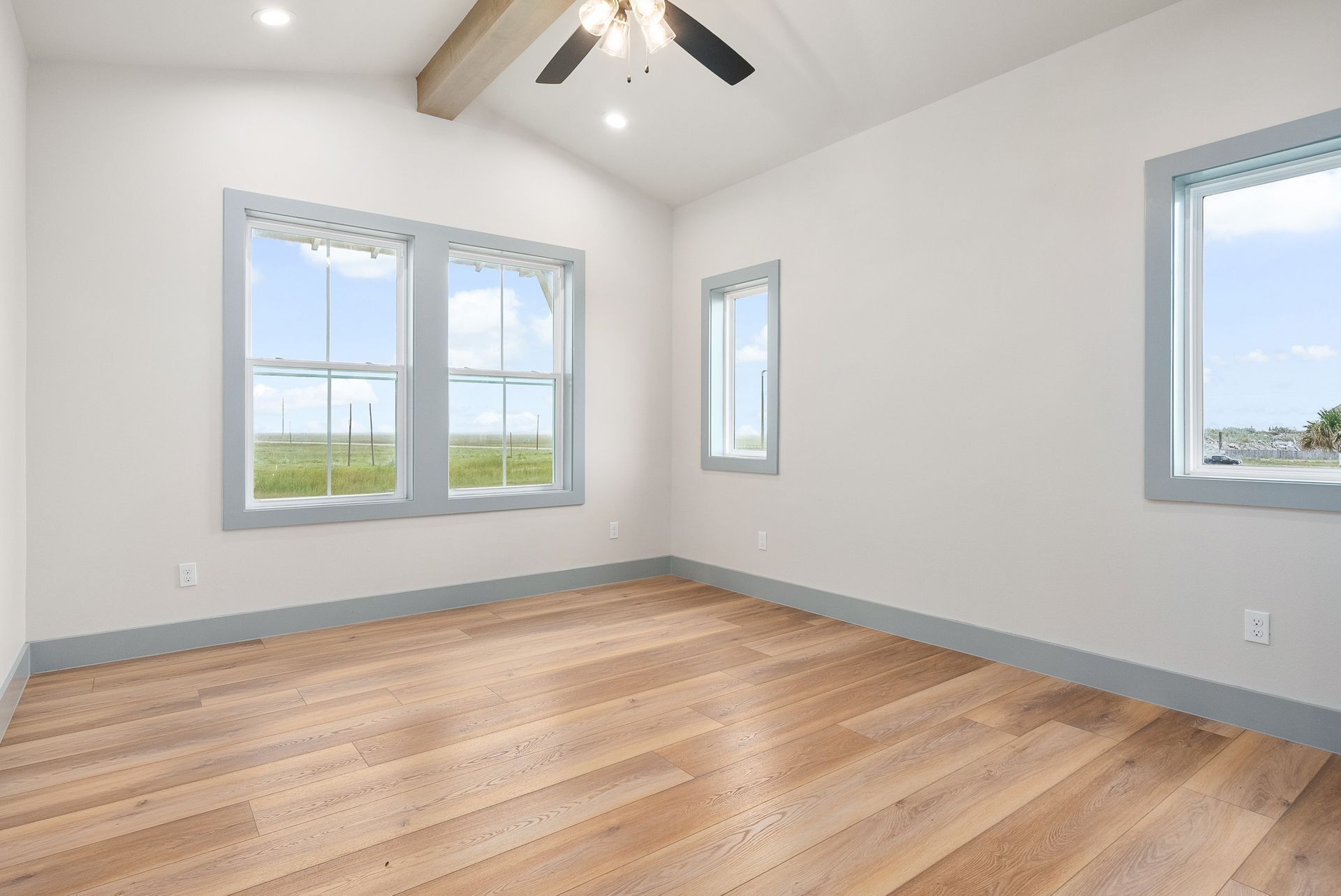 Empty room with light wood floor, white walls, blue window frames, and ceiling fan.