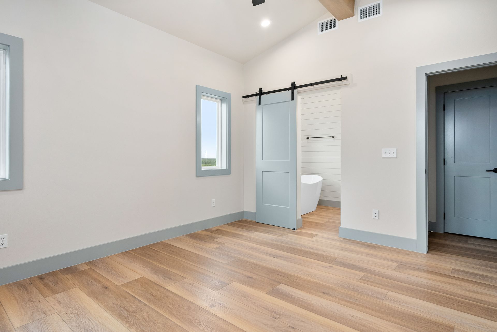 Empty bedroom with wooden floor, light blue accents on doors and trim, and a sliding door.