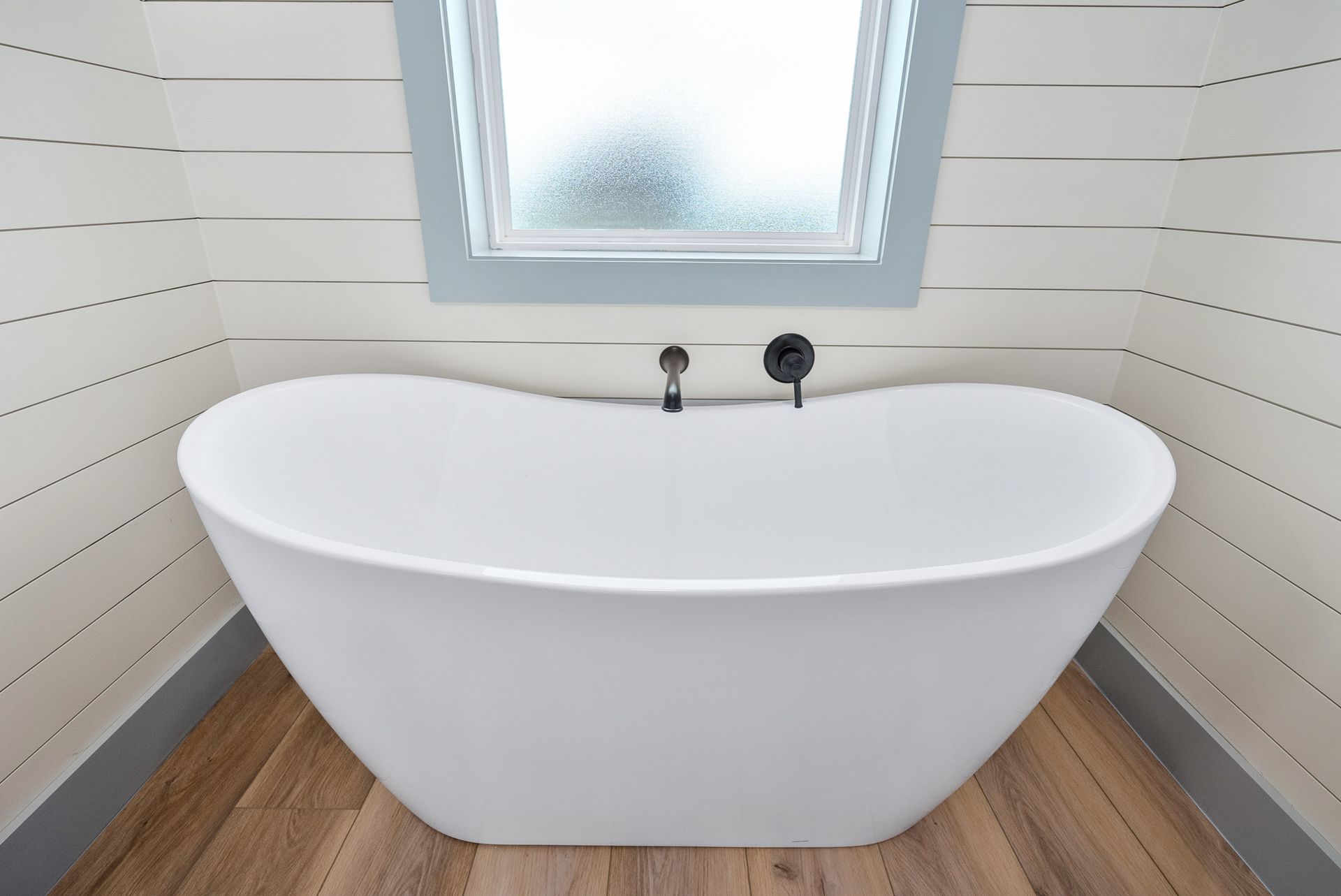 White, freestanding bathtub in a bathroom with shiplap walls and a frosted window.