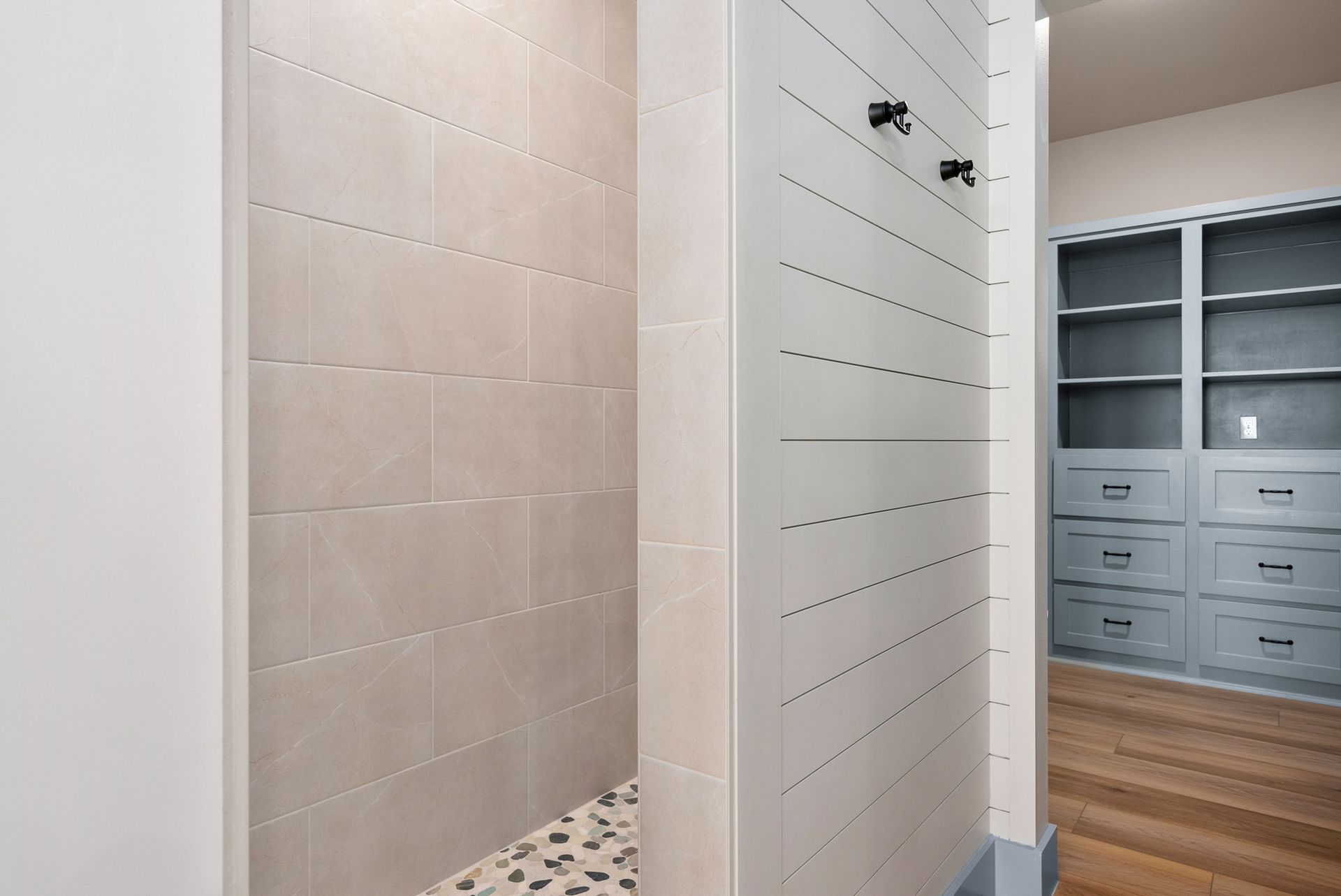 Bathroom interior: tiled shower on left, white paneled wall with hooks, gray cabinets on right.