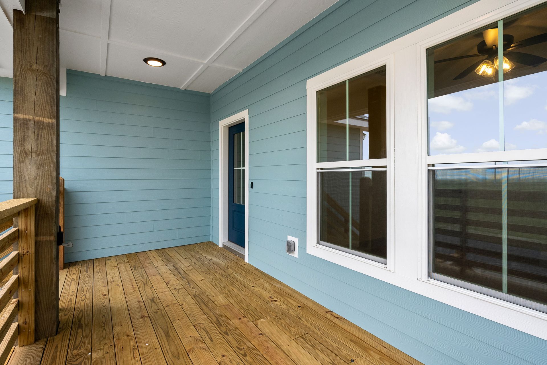 Blue porch with wooden deck and white-framed windows, door, and ceiling light.