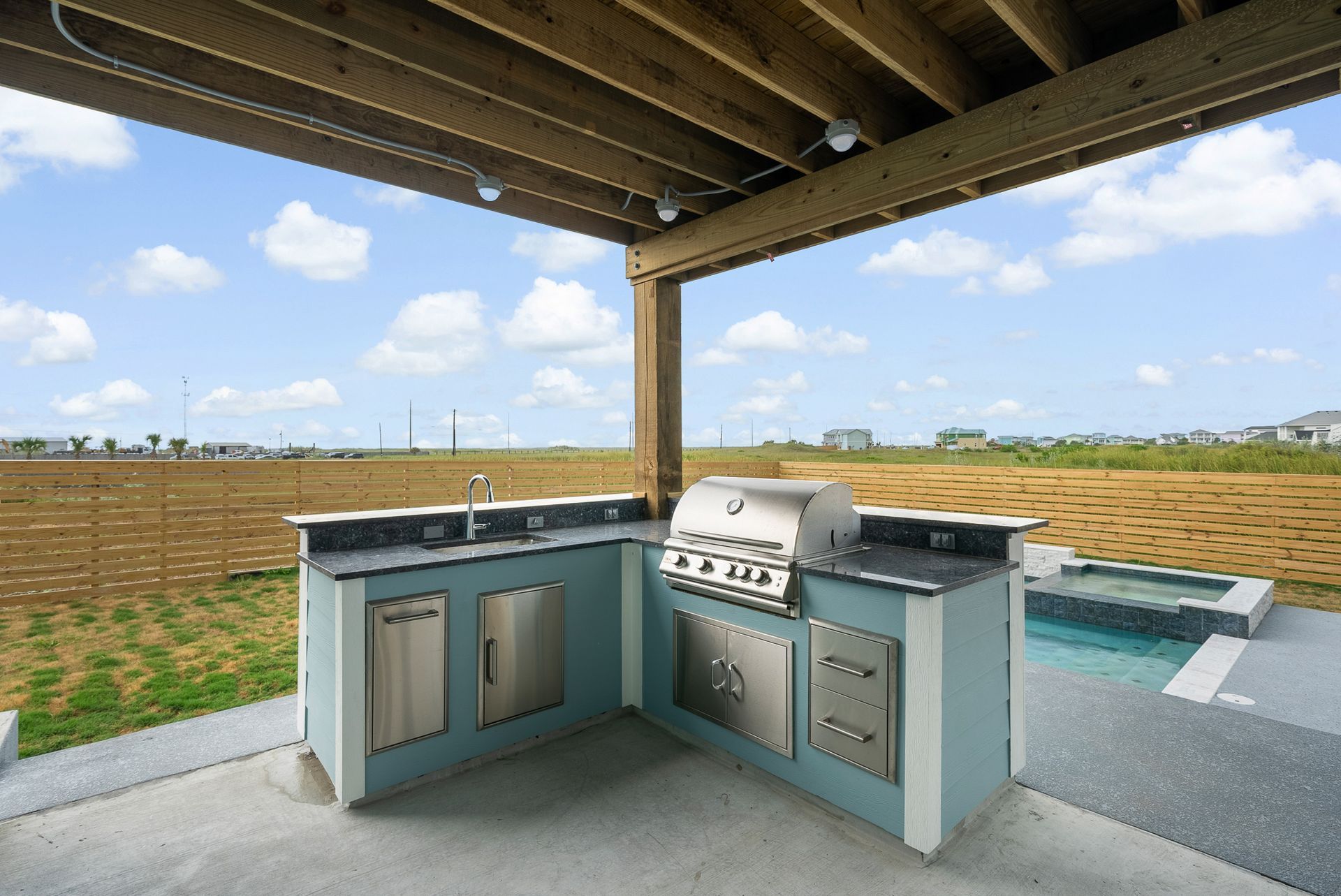 Outdoor kitchen with grill, sink, storage, and small hot tub under a wooden roof.