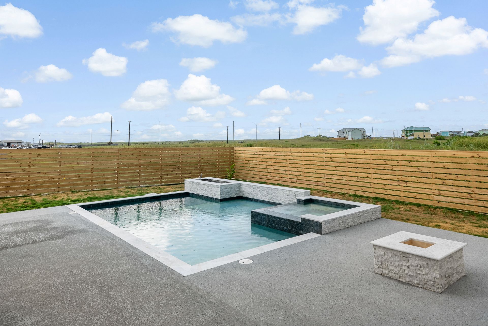 Small pool and fire pit area with stone features; a bermed hillside in the background under a blue sky.