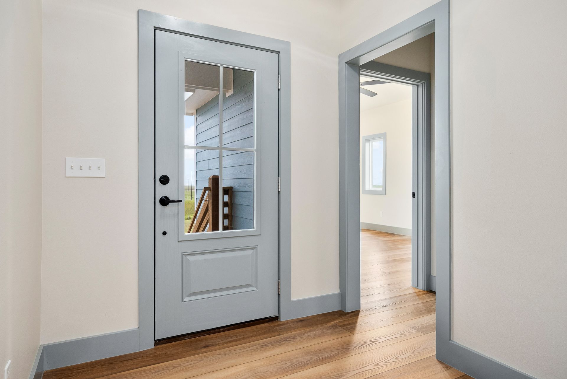 Blue door with glass panels and gray trim in a hallway, leading to another room.
