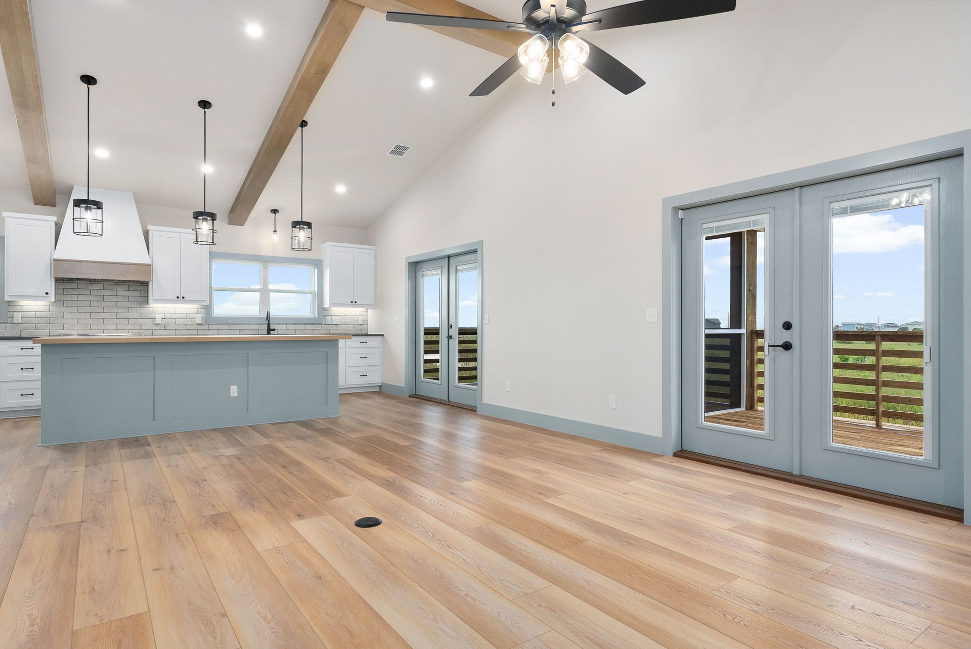 Open-concept kitchen and living area with wooden floors, blue cabinetry, and outdoor access through double doors.