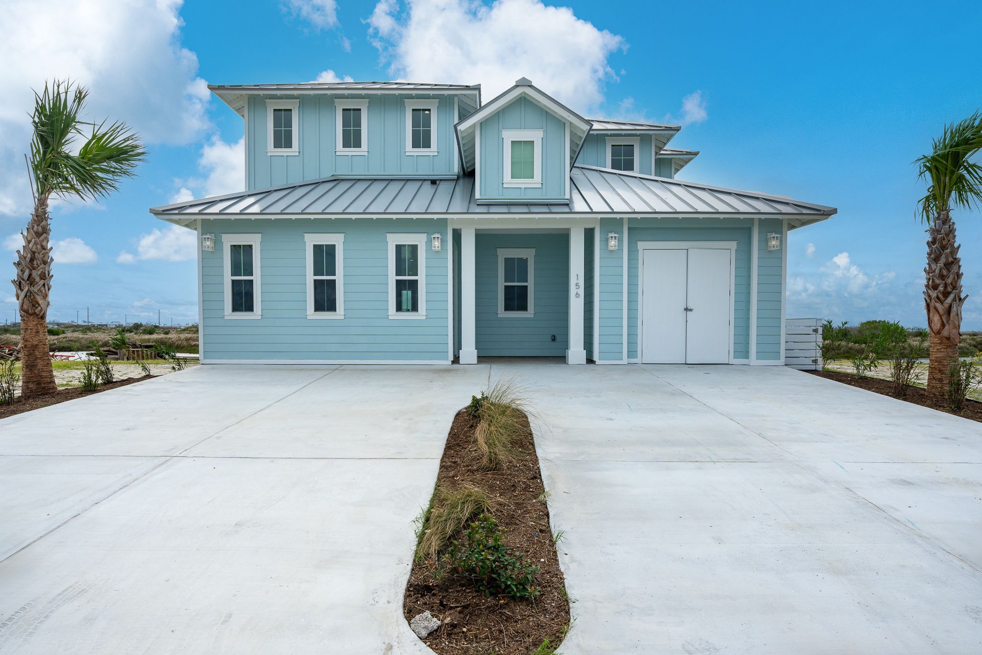 A large house with a concrete driveway and palm trees in front of it