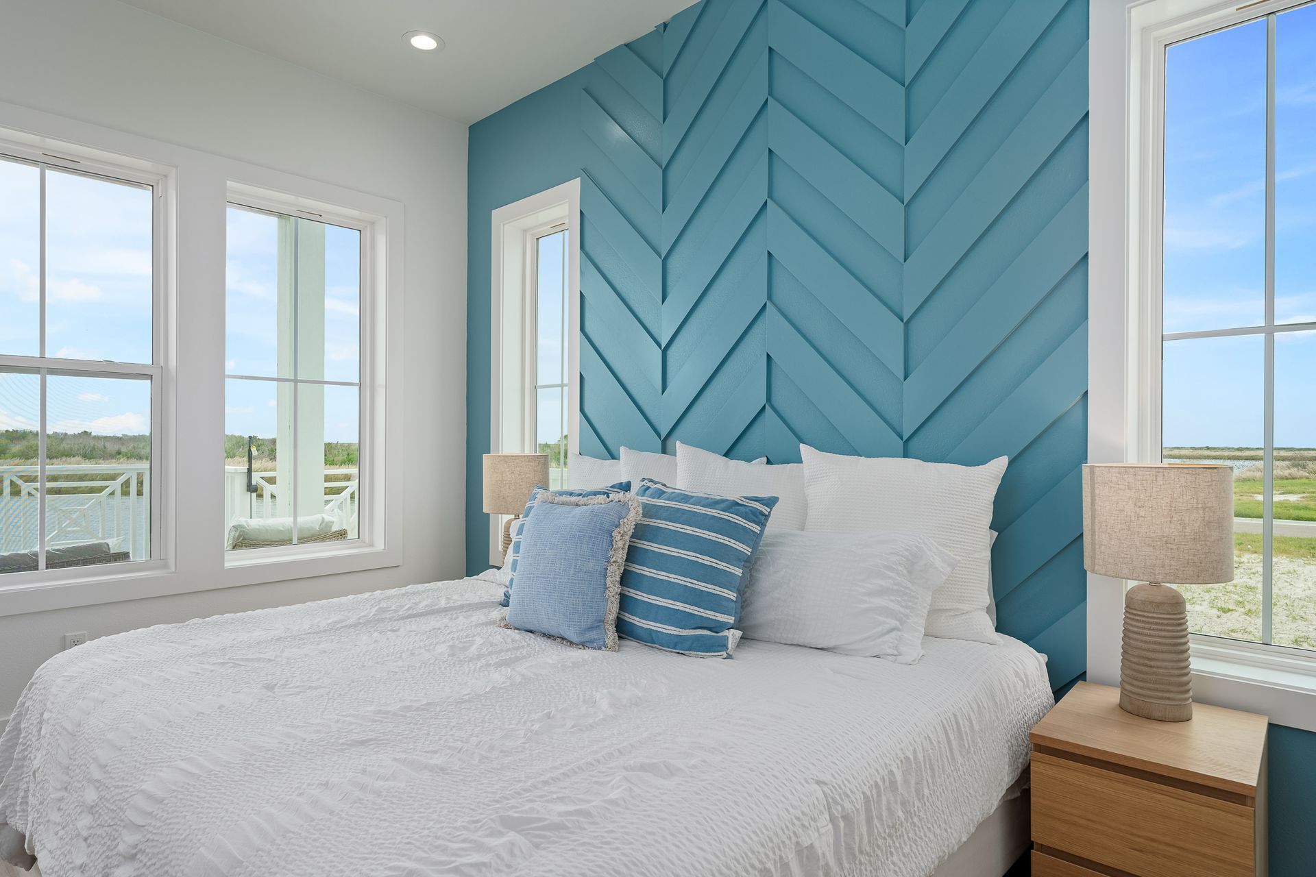 A bedroom with a bed , nightstand , lamps and a blue wall.
