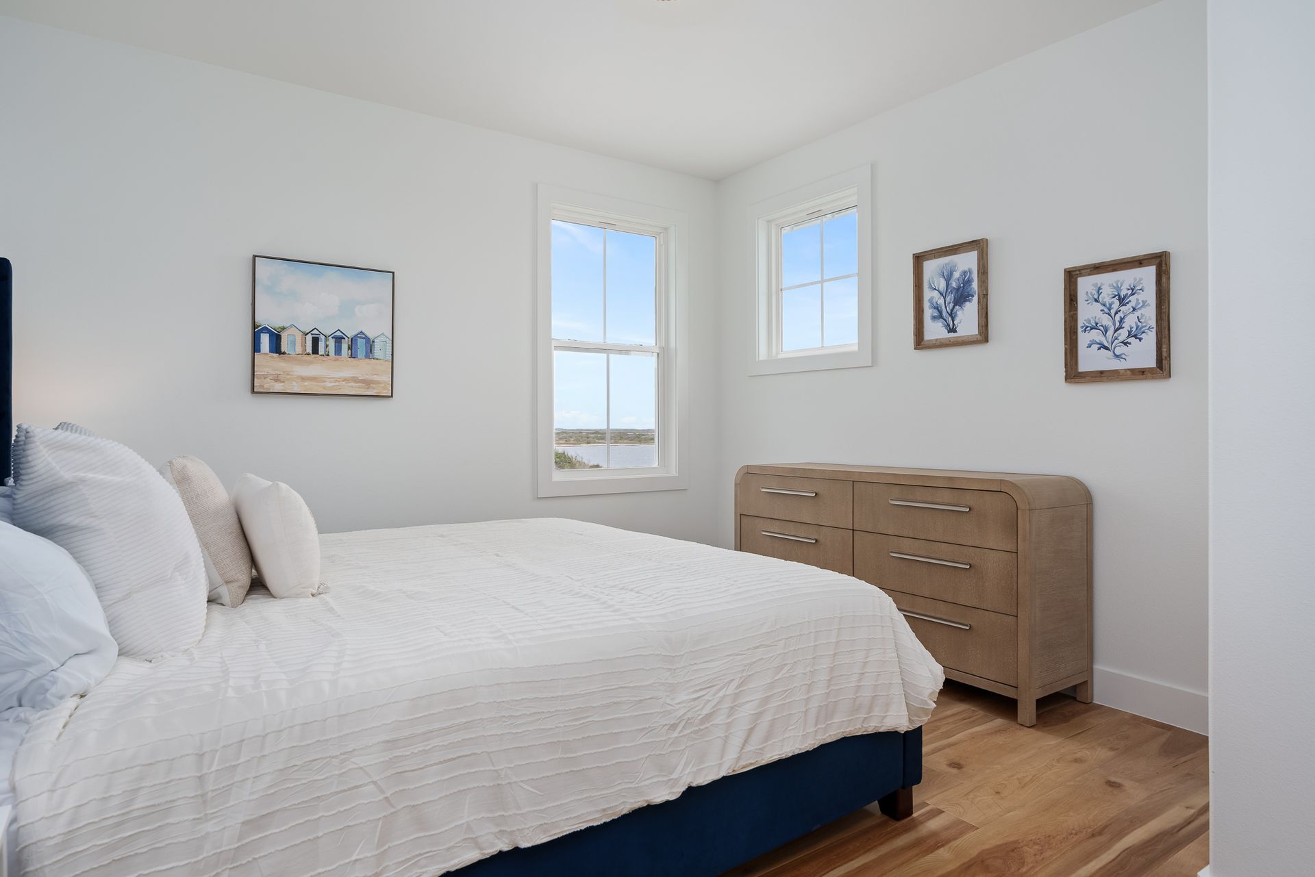 A bedroom with a bed , dresser , and two windows.