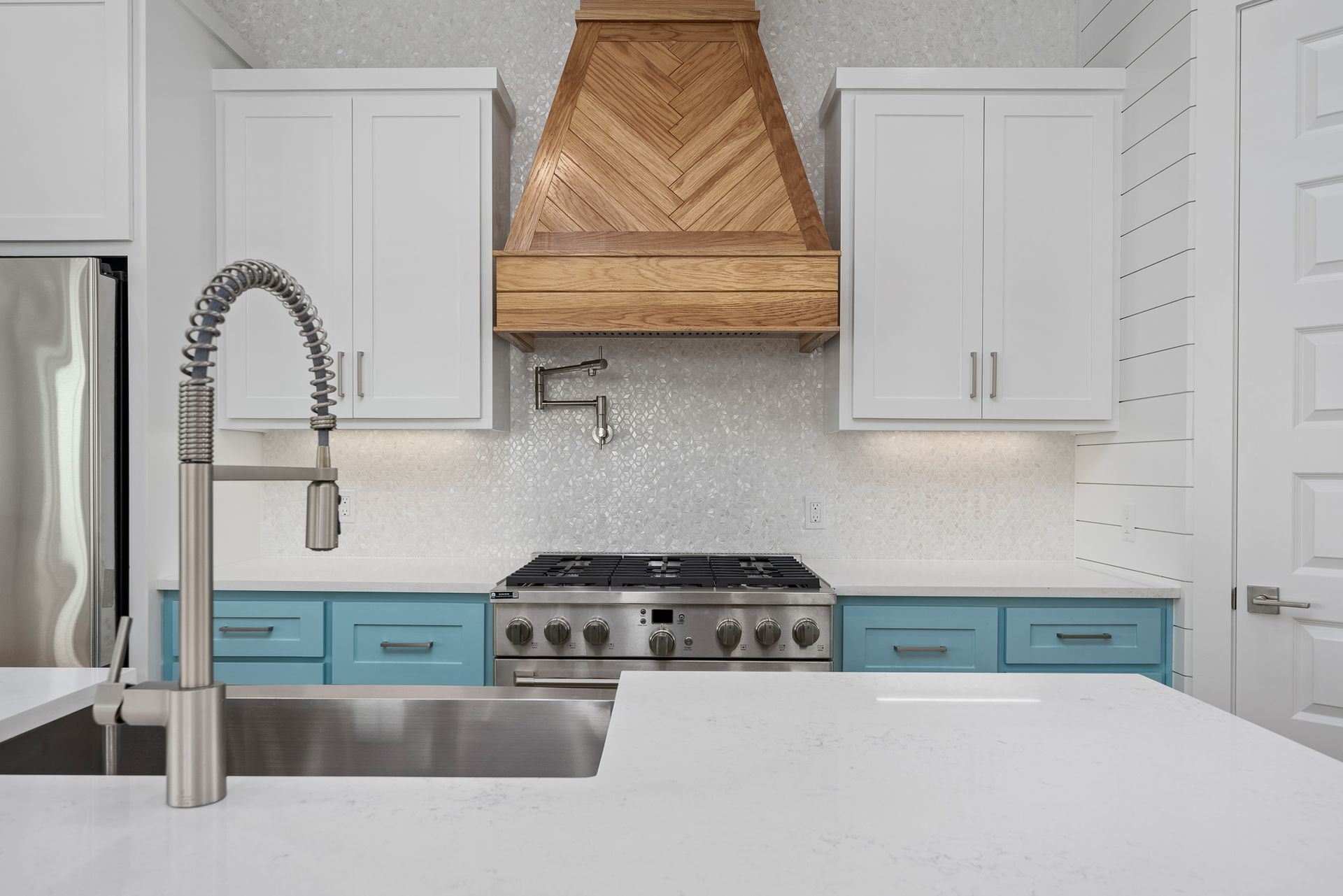 A kitchen with white cabinets , blue cabinets , stainless steel appliances , a sink and a stove.