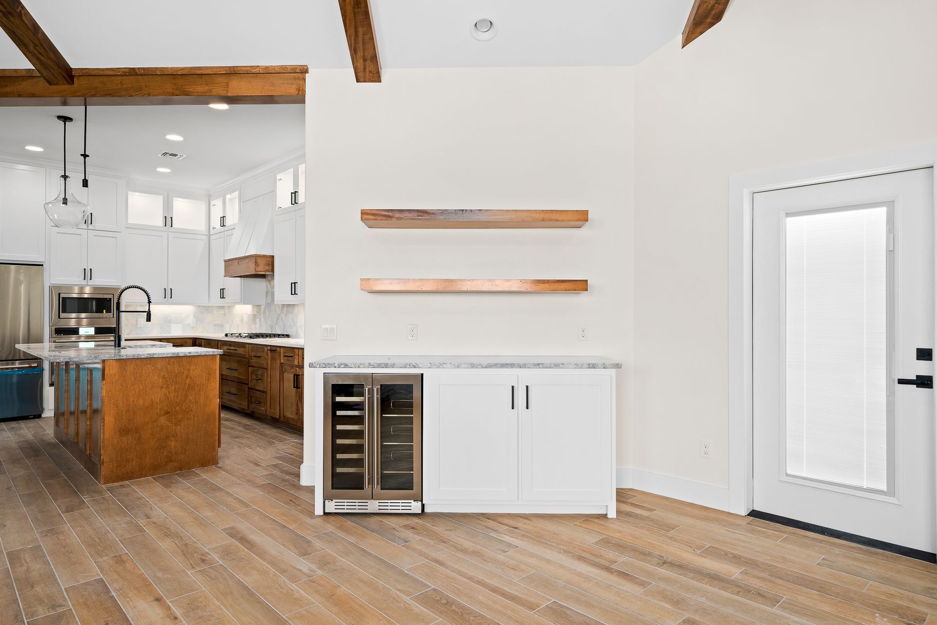 A kitchen with wooden floors , white cabinets , stainless steel appliances and a refrigerator.