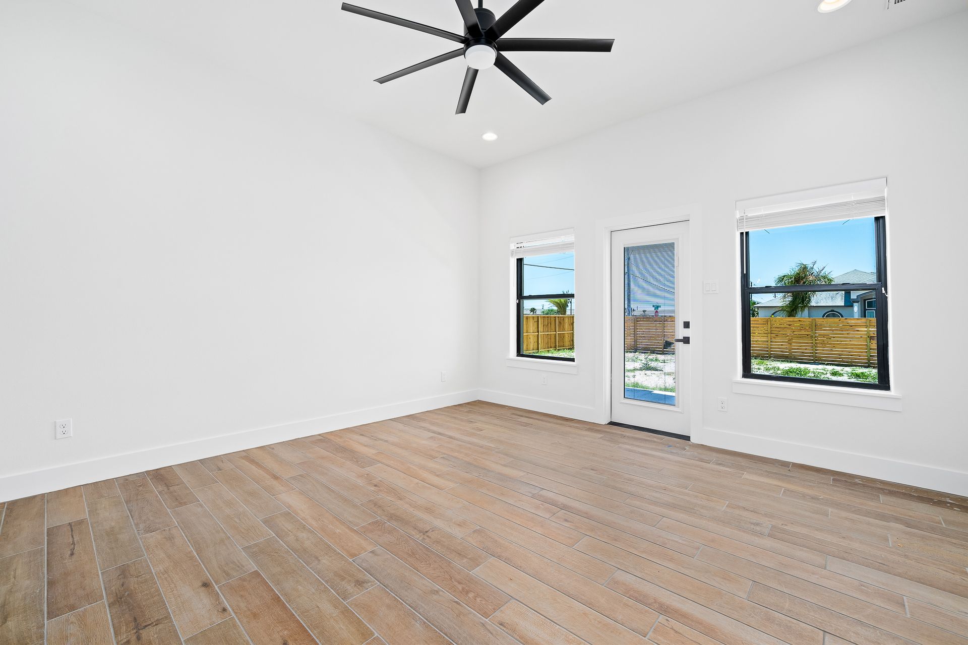 An empty living room with wooden floors and a ceiling fan.