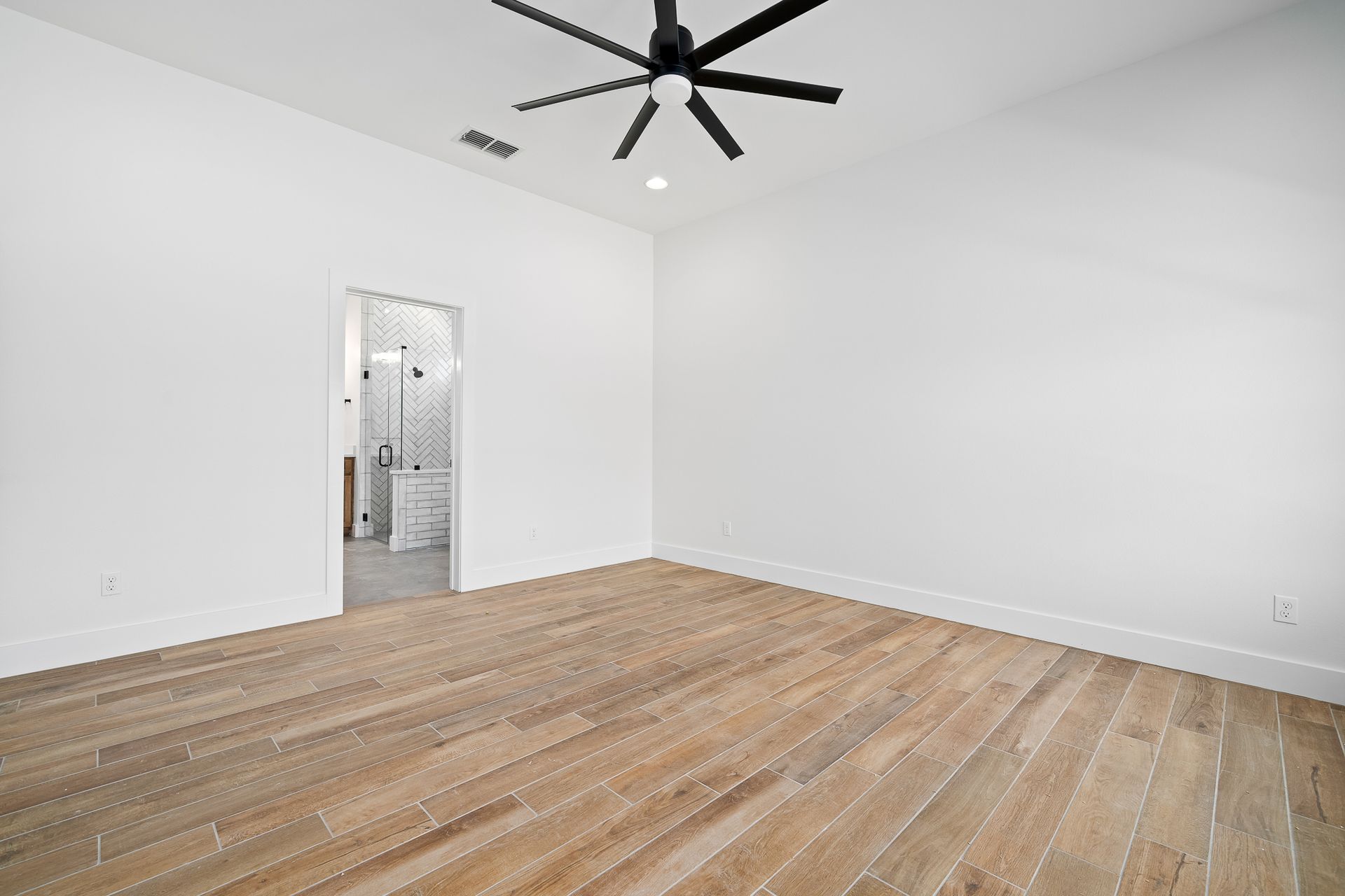 An empty room with wooden floors and a ceiling fan.