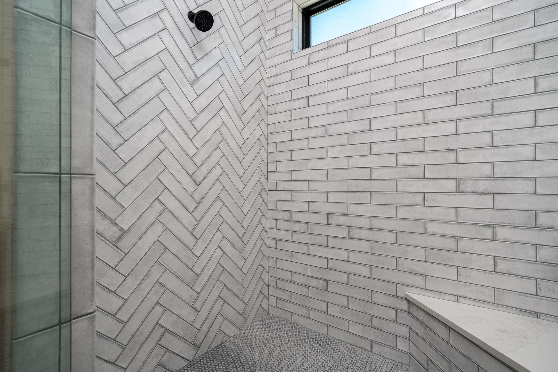 A shower with a herringbone pattern on the wall and a window.