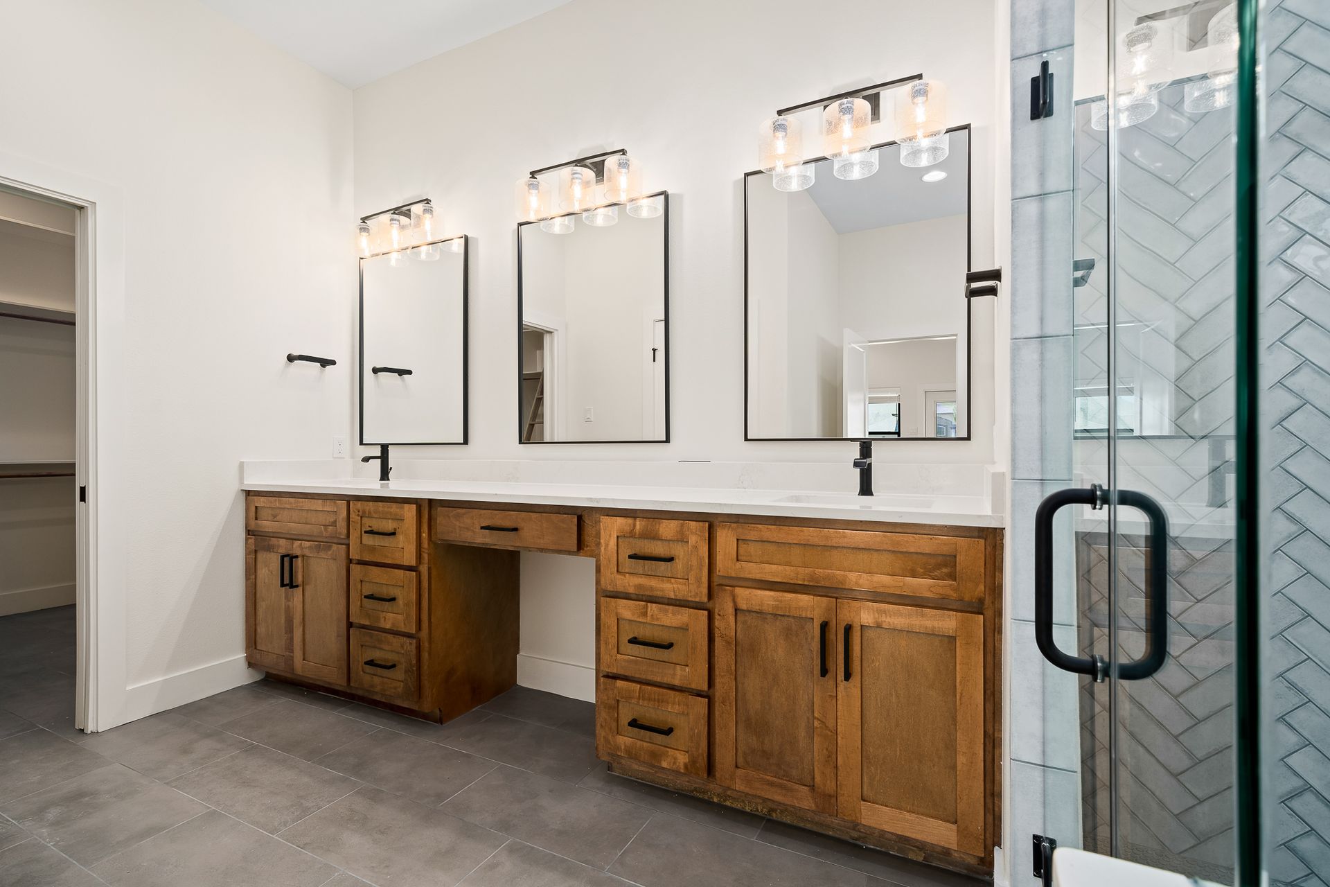 A bathroom with two sinks , two mirrors , and a walk in shower.