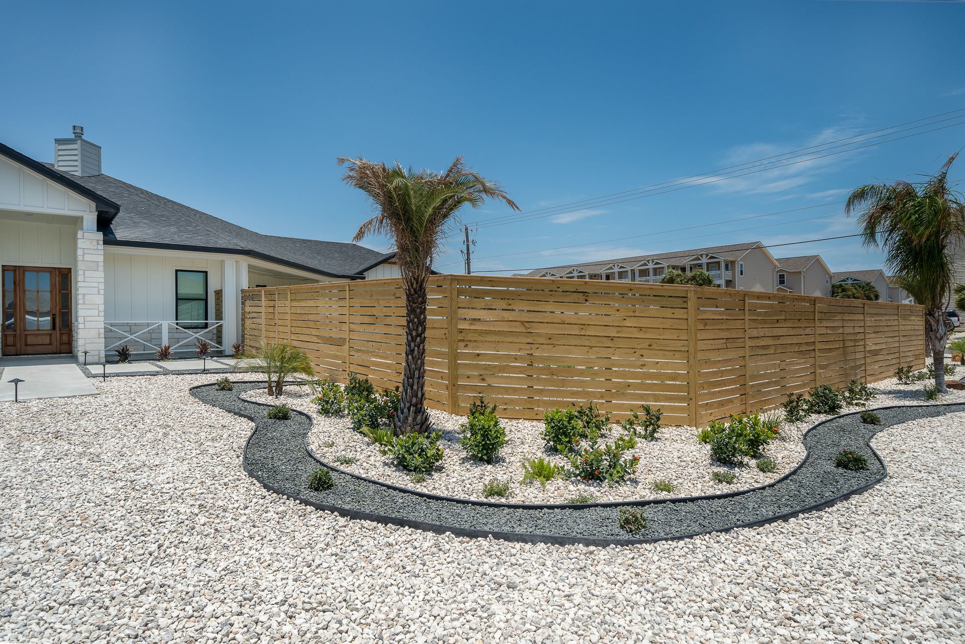 A house with a wooden fence and gravel in front of it.