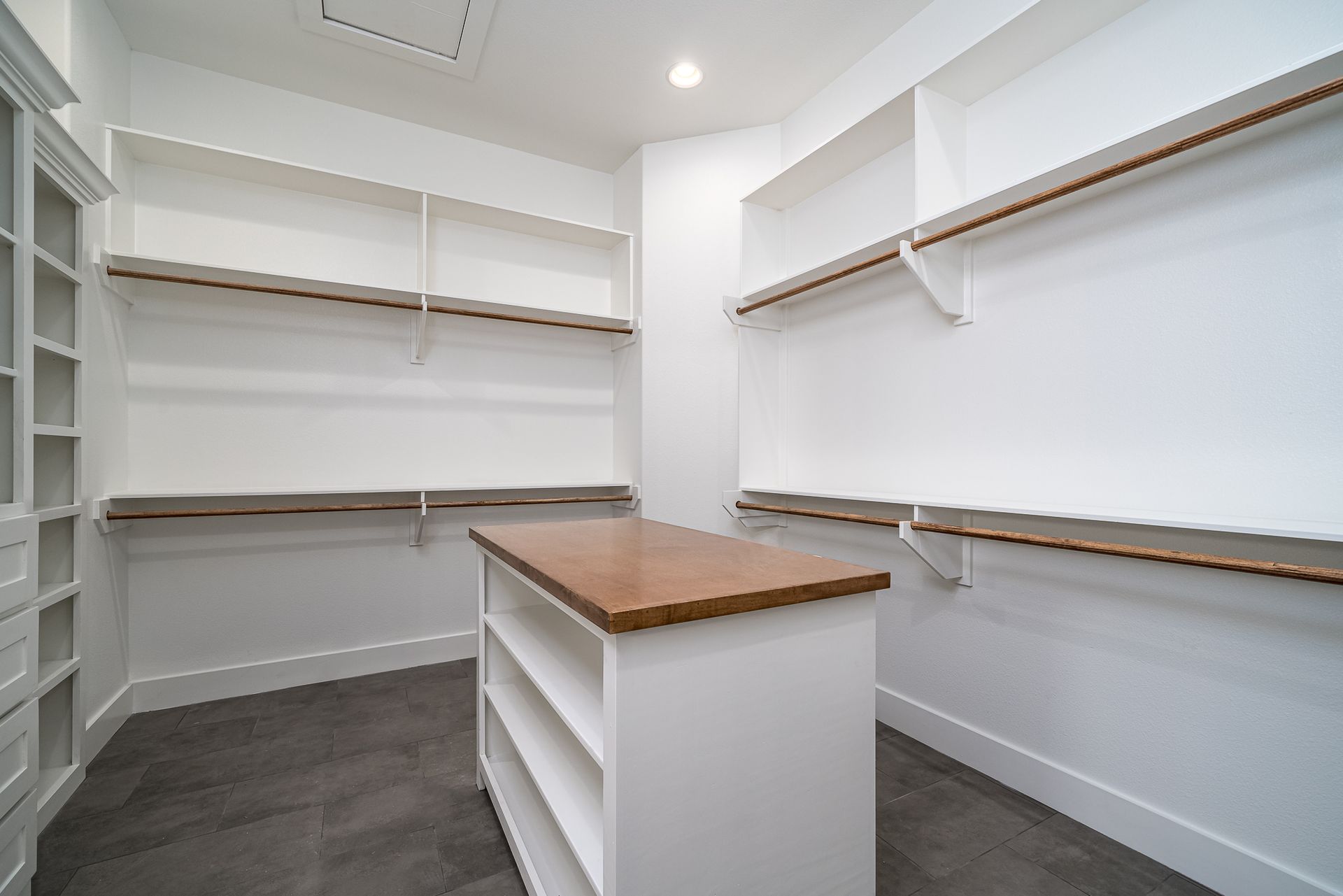 An empty walk in closet with white shelves and a wooden table.