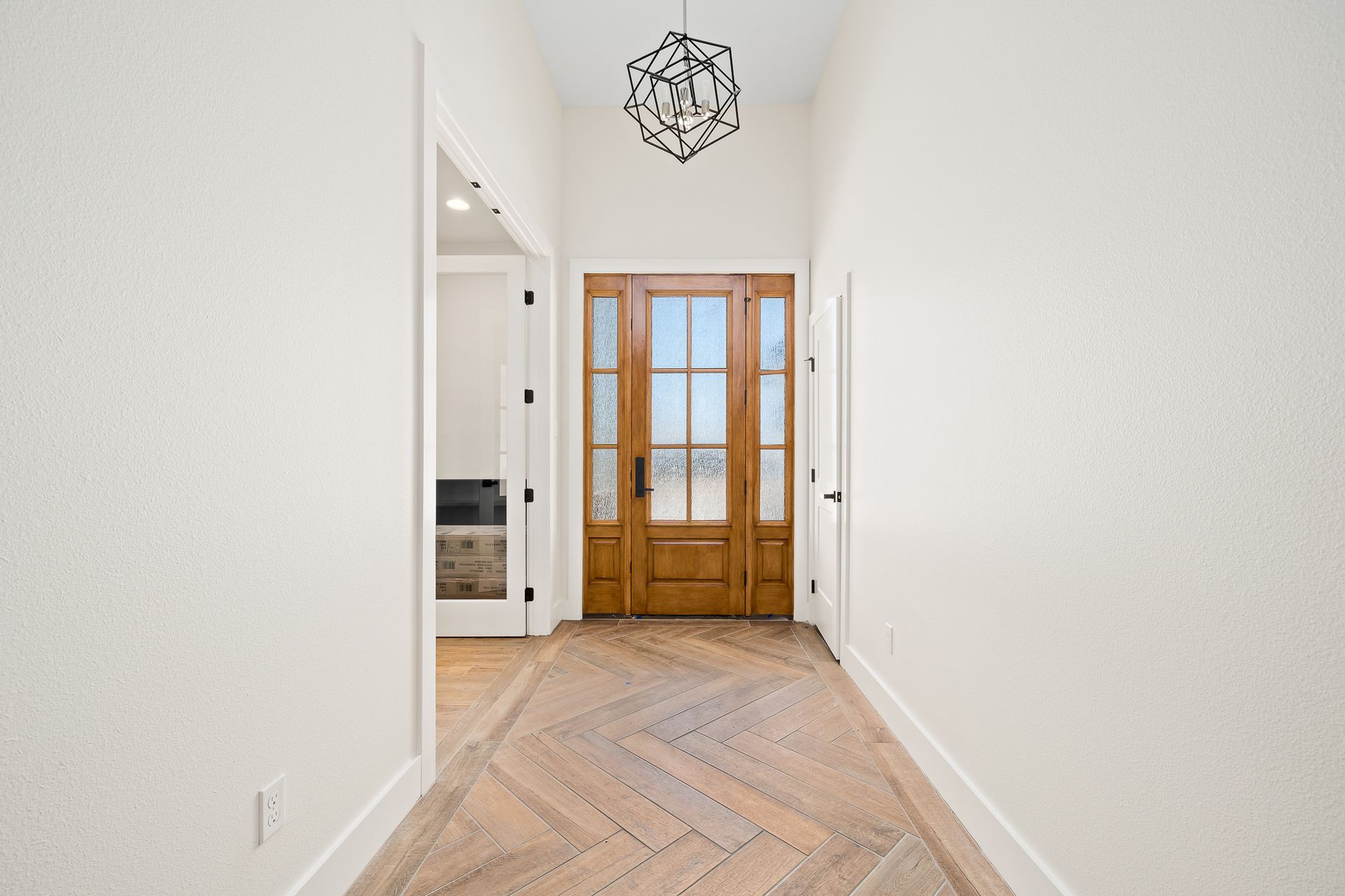 A hallway with a wooden door and a chandelier hanging from the ceiling.