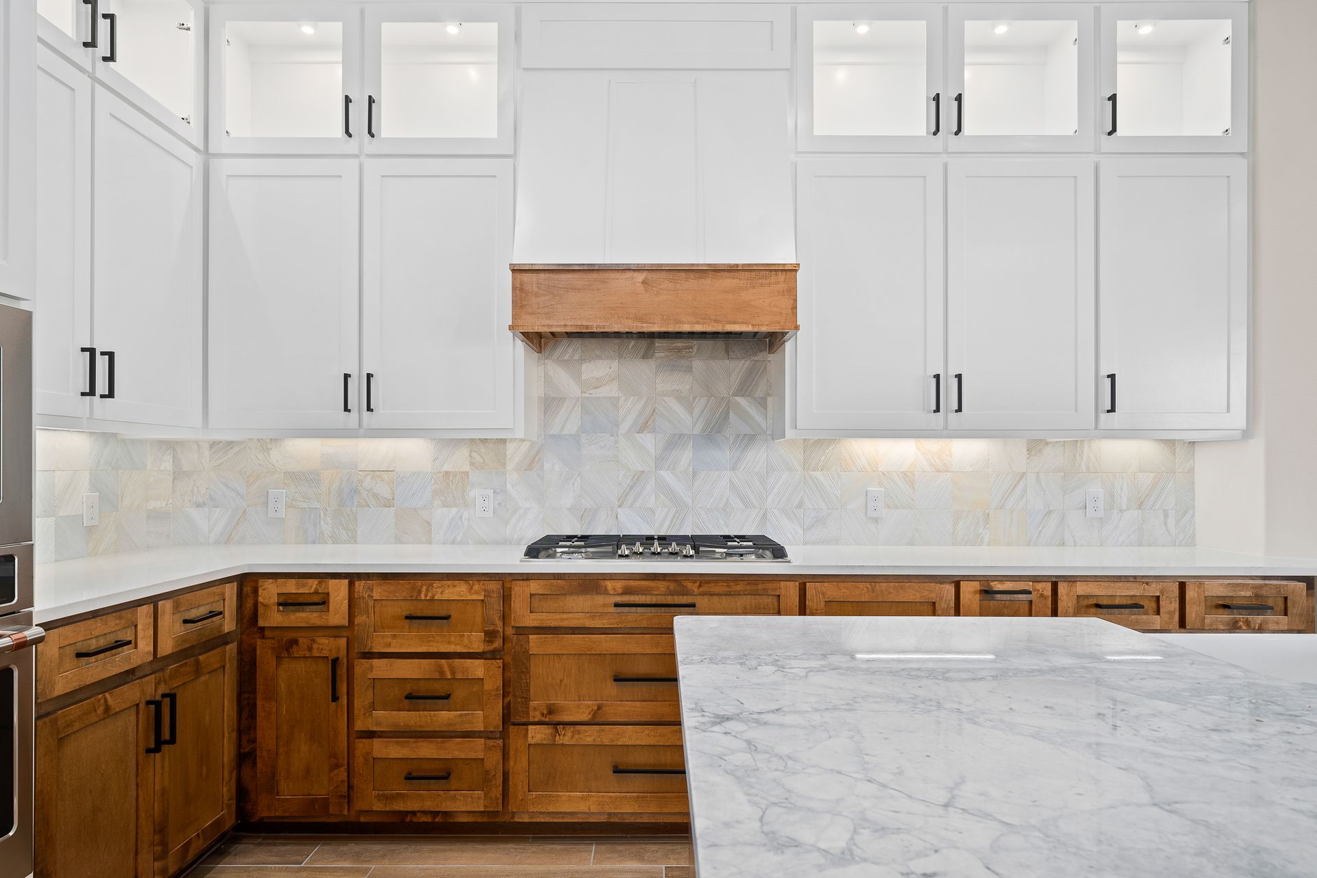 A kitchen with white cabinets and wooden cabinets and a marble counter top.