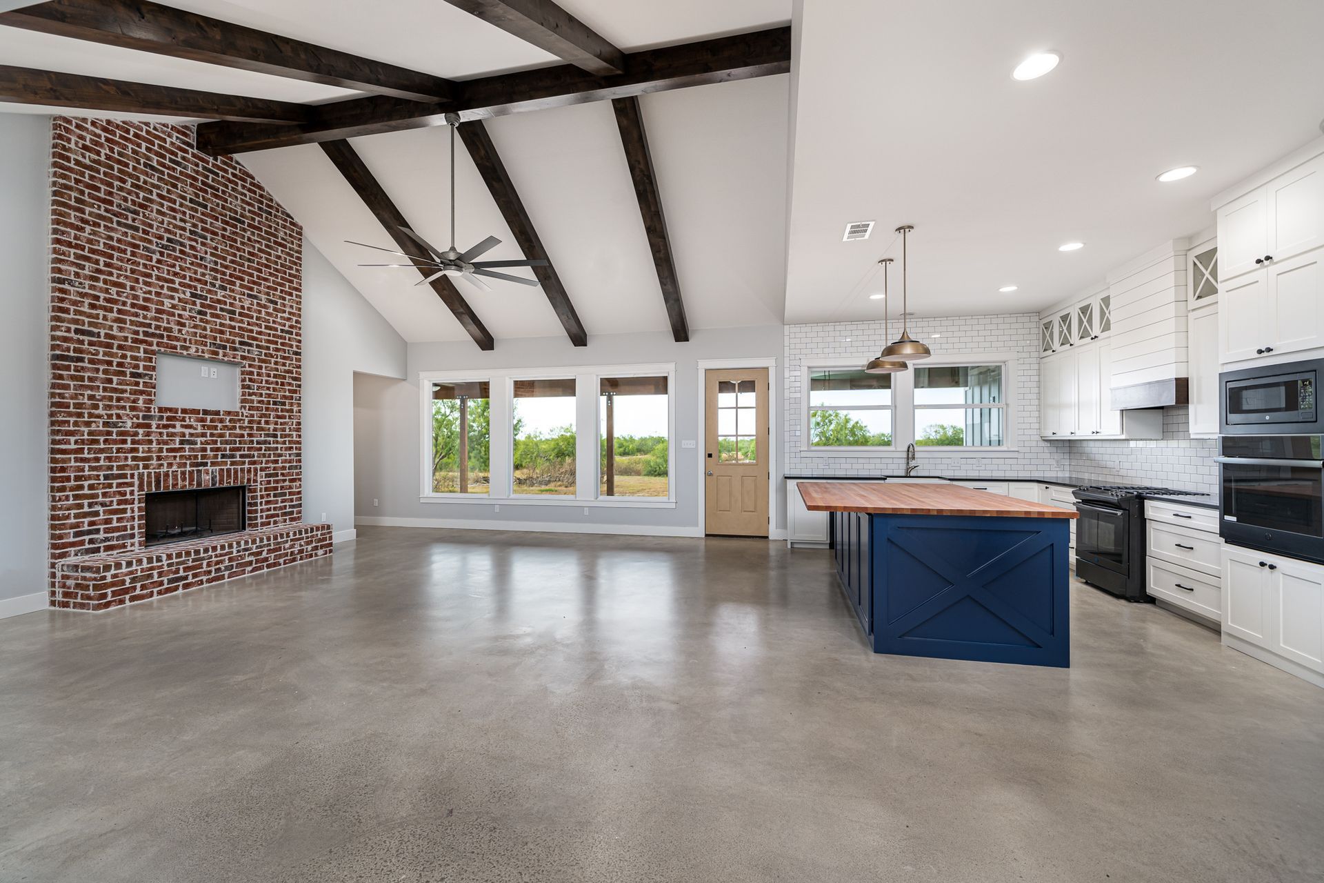 An empty kitchen with a blue island and a brick fireplace