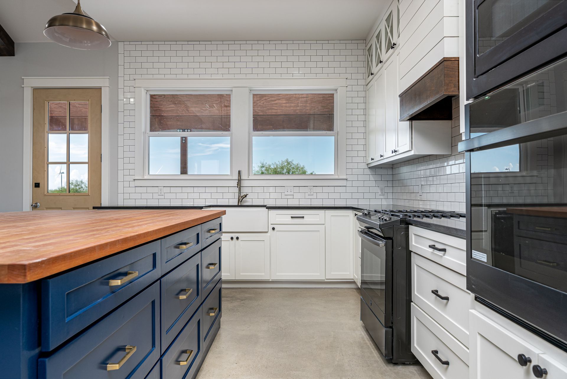A kitchen with white cabinets , black appliances , and a blue island.