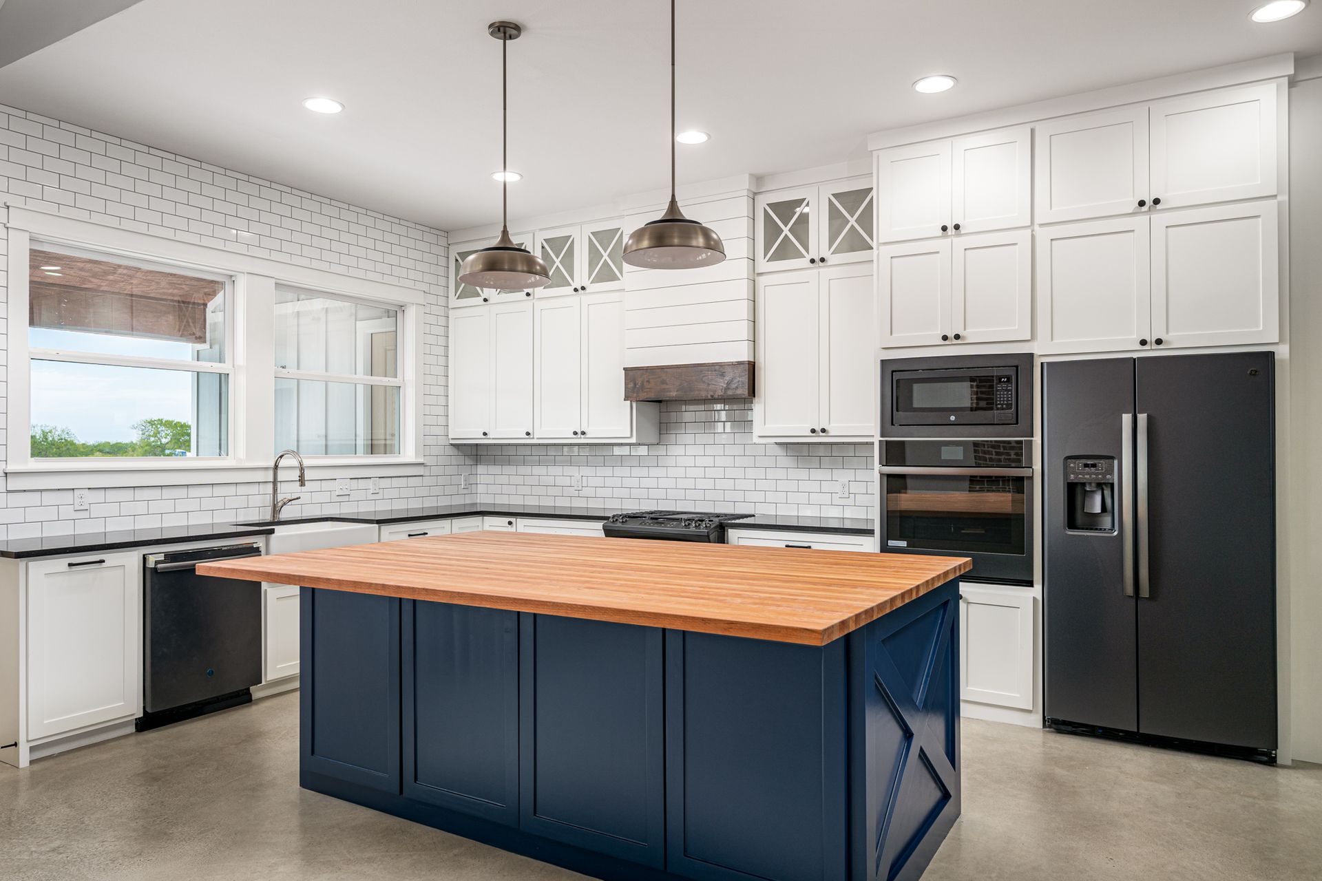 A kitchen with white cabinets , black appliances , and a large blue island.