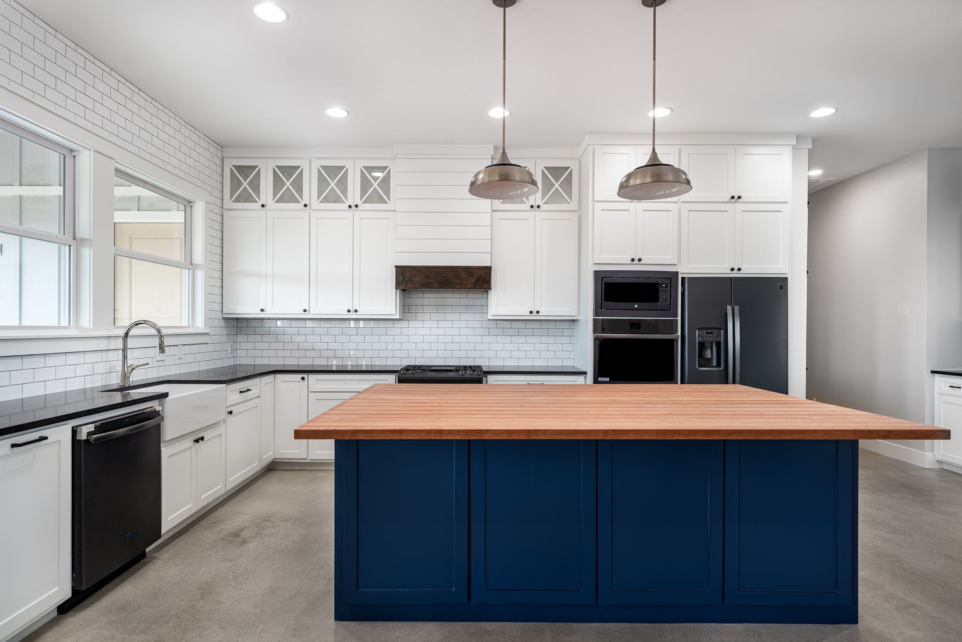 A kitchen with white cabinets , black appliances , a blue island and a wooden counter top.