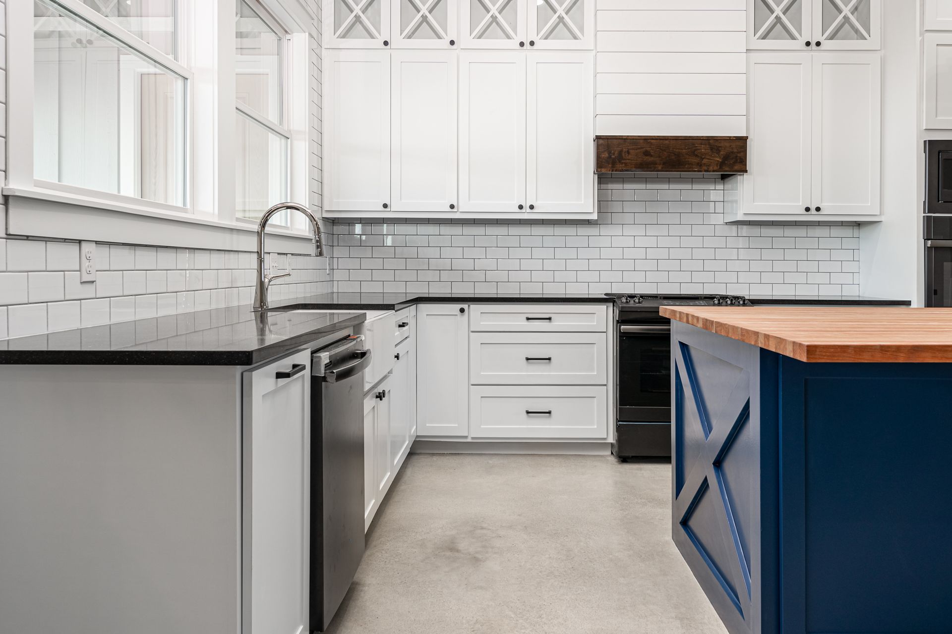 A kitchen with white cabinets , black counter tops , and a blue island.