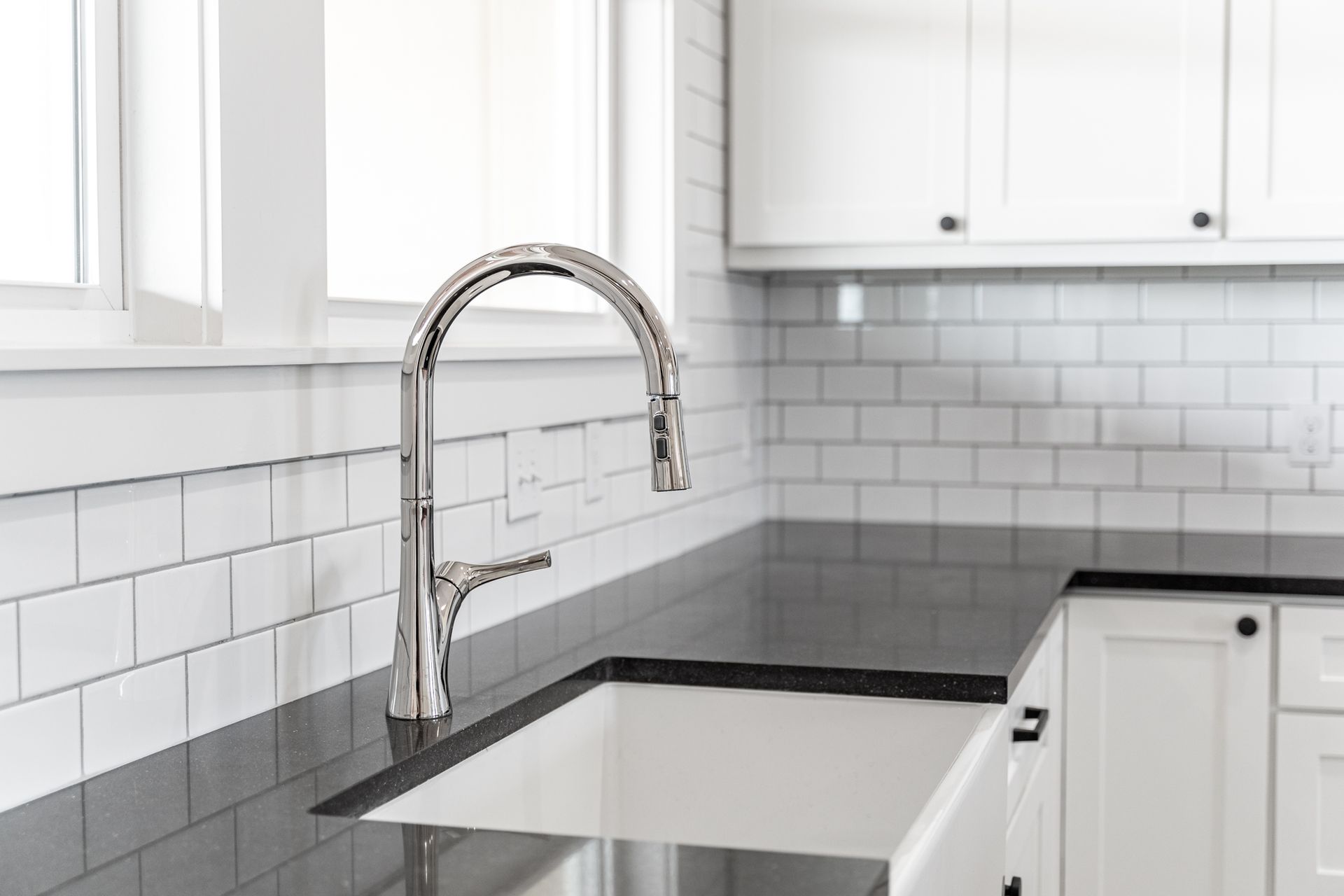 A kitchen sink with a faucet and black counter tops.