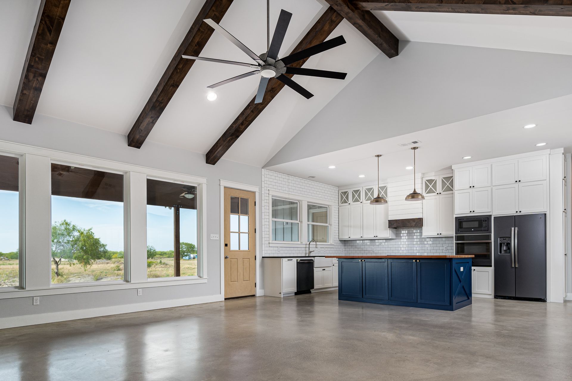 A large empty room with a kitchen and a ceiling fan