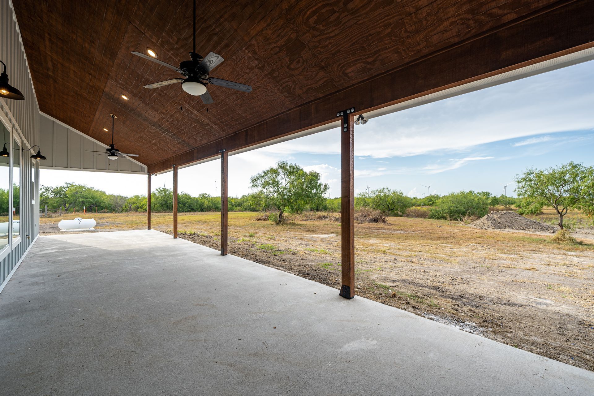 A large covered patio with a ceiling fan and a view of a field.