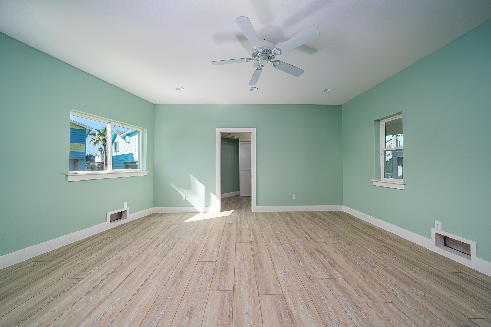 An empty room with a ceiling fan and two windows.