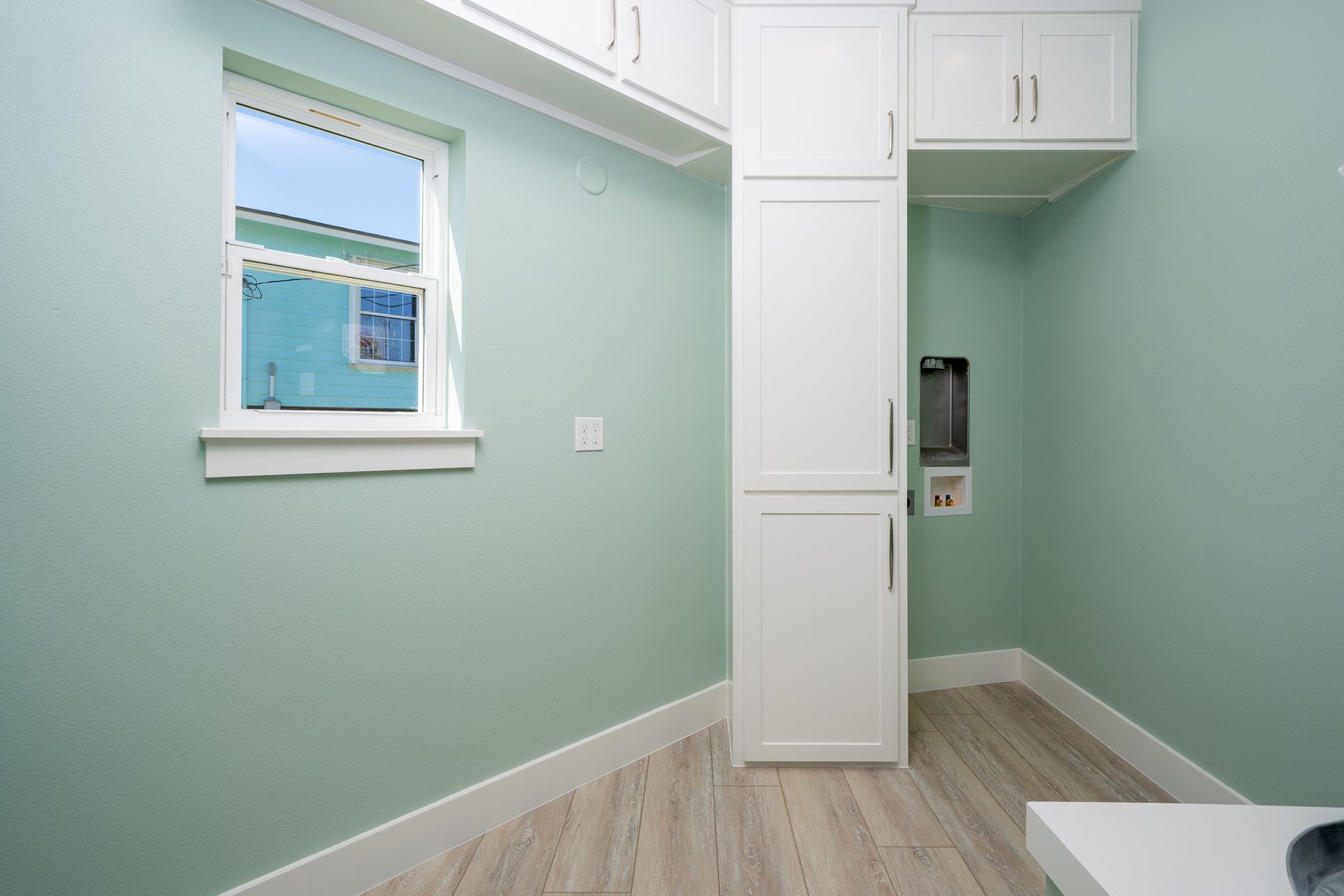 A room with green walls and white cabinets and a window.