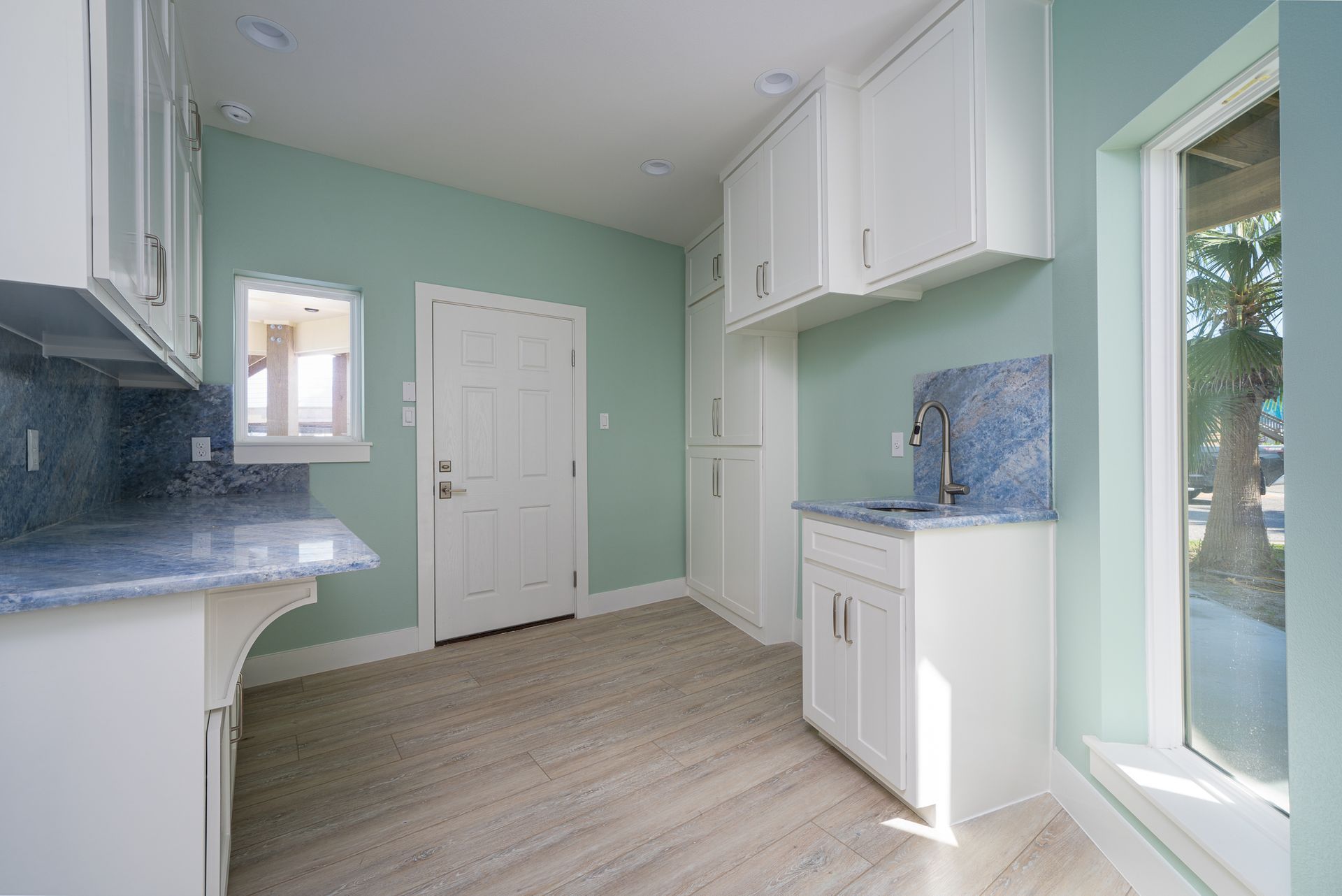 An empty kitchen with white cabinets , a sink , and a window.