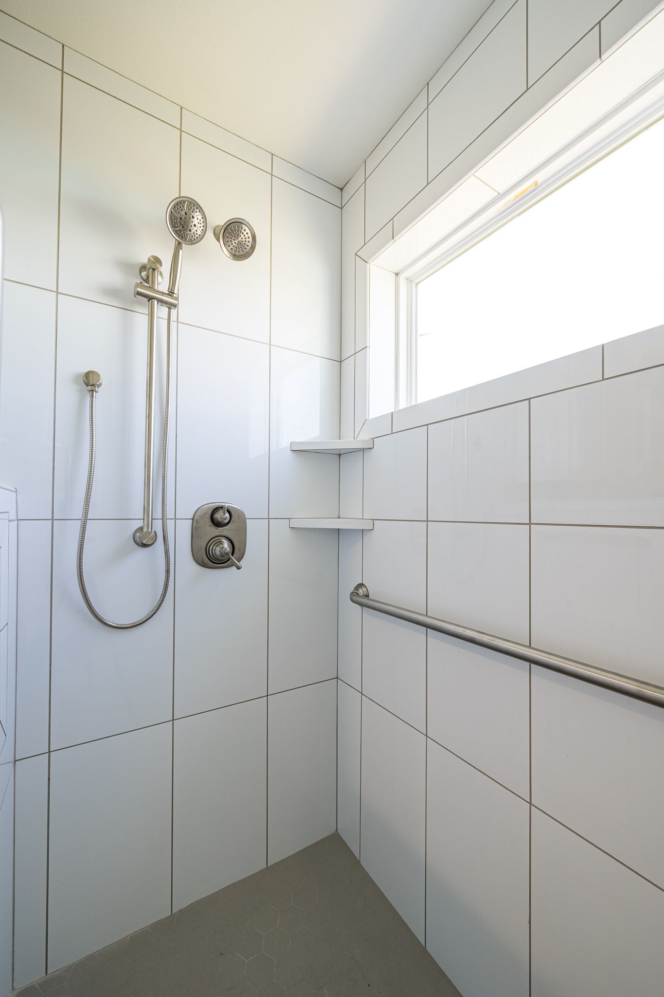 A shower with white tiles and a window.
