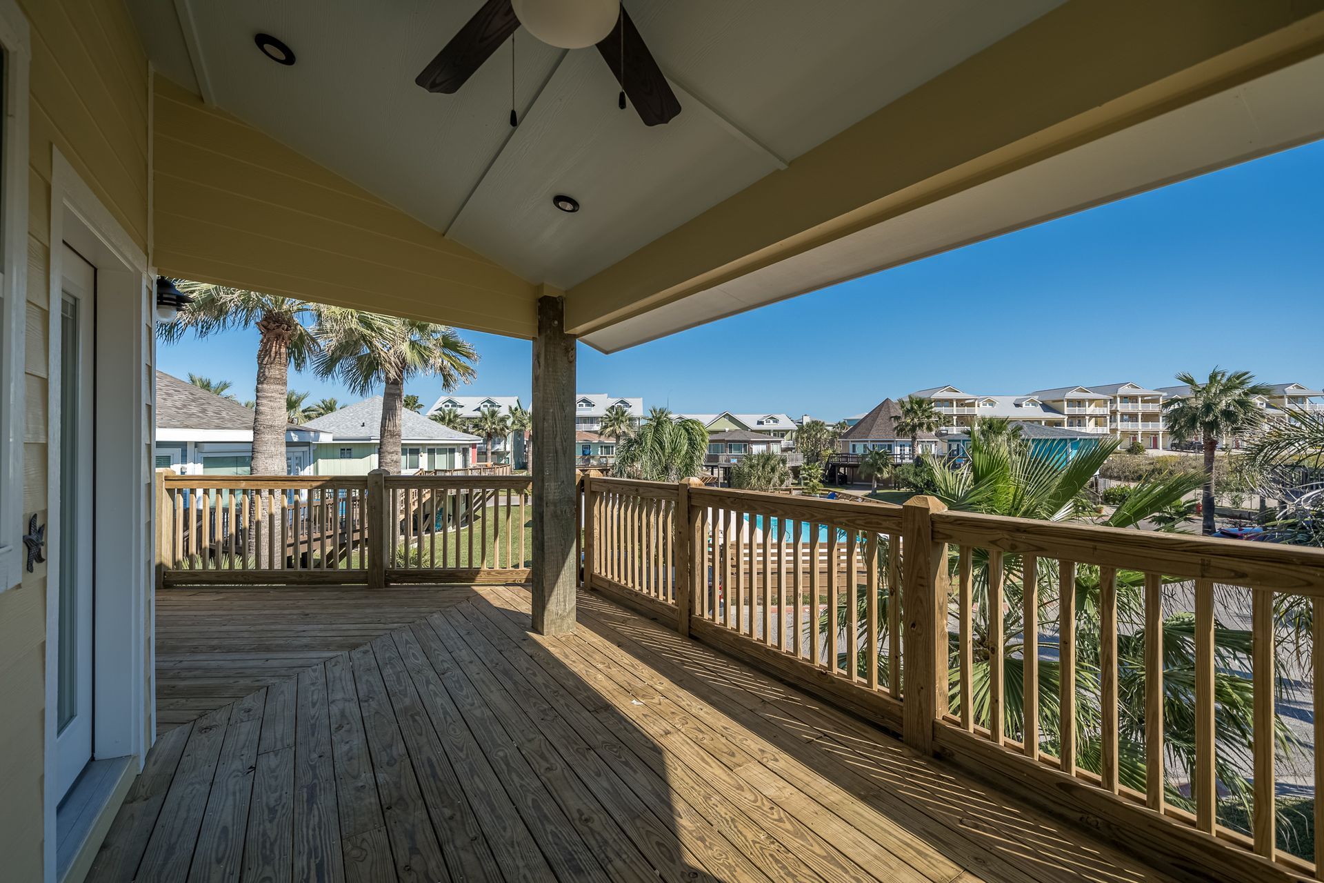 An empty deck with a wooden railing and a ceiling fan.