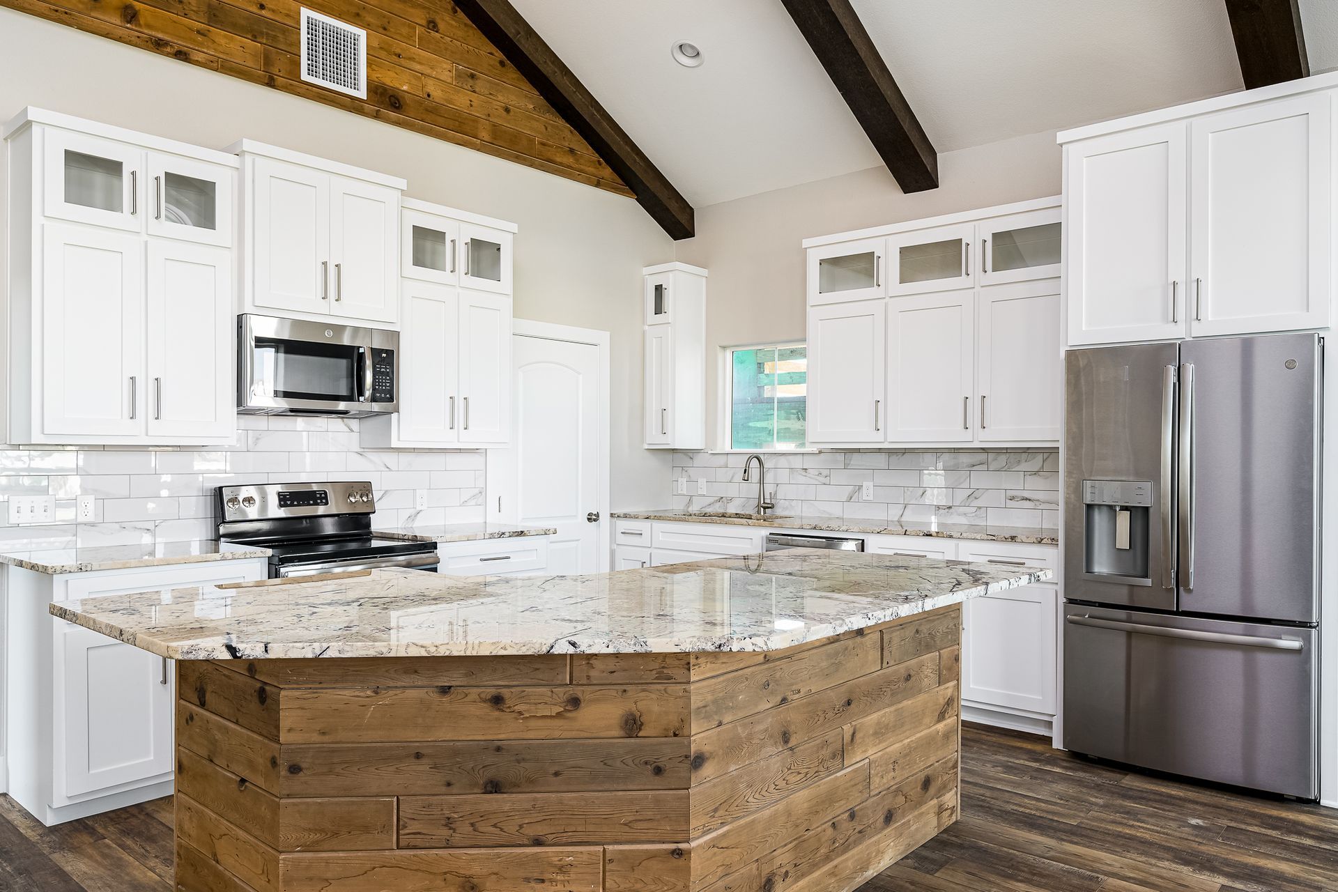A kitchen with white cabinets , granite counter tops , stainless steel appliances and a wooden island.