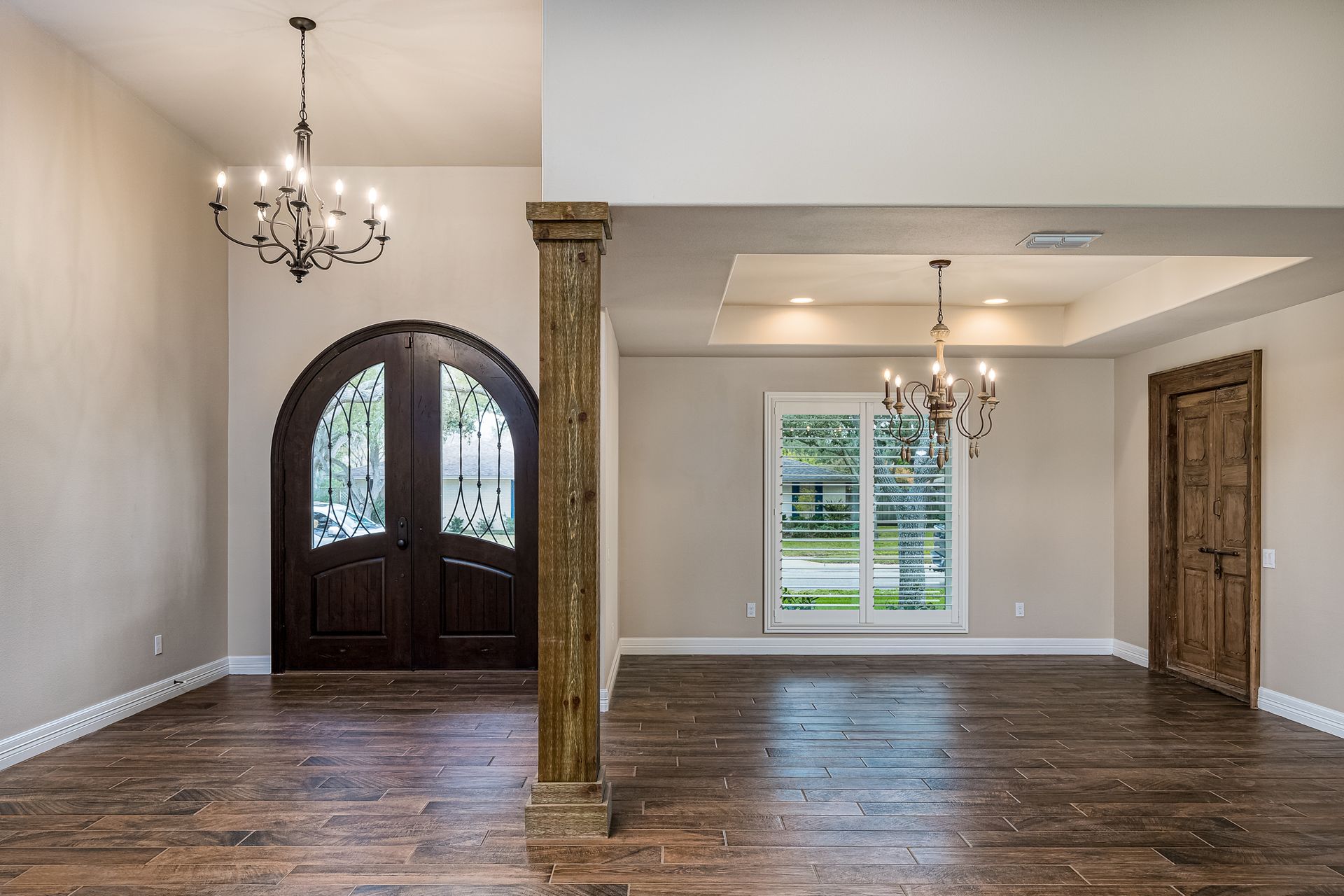 A large empty room with hardwood floors and a chandelier hanging from the ceiling.