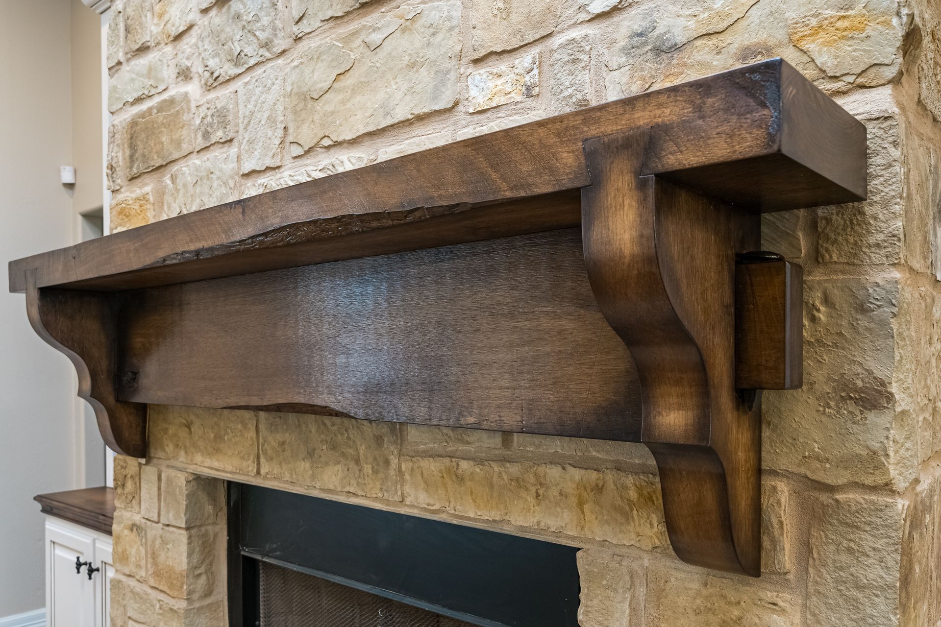 A wooden mantle is sitting on top of a stone fireplace.