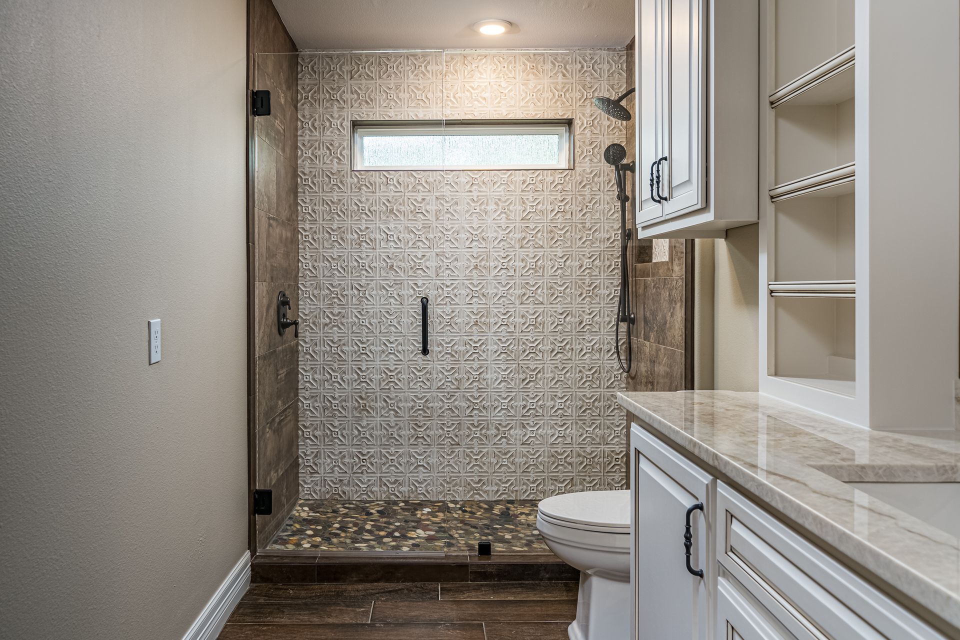 A bathroom with a walk in shower , toilet , sink and cabinets.