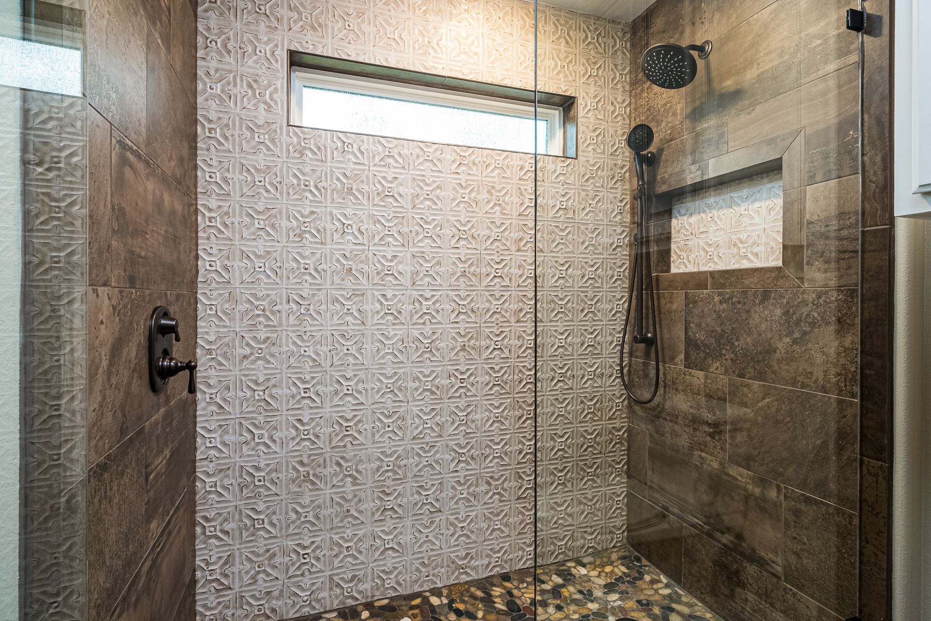 A walk in shower with a glass door and a window.